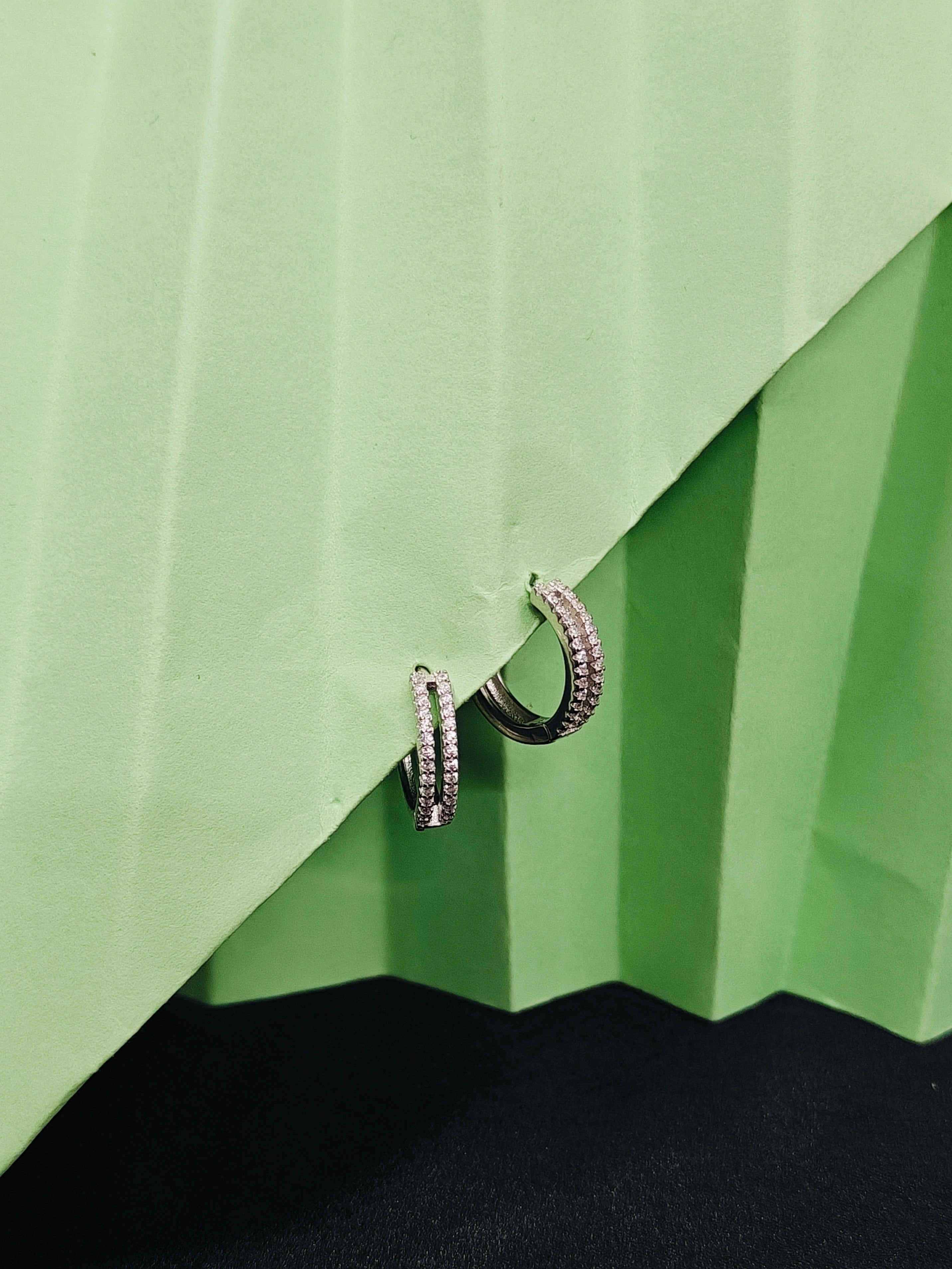 Pair of silver hoop earrings on a green textured surface