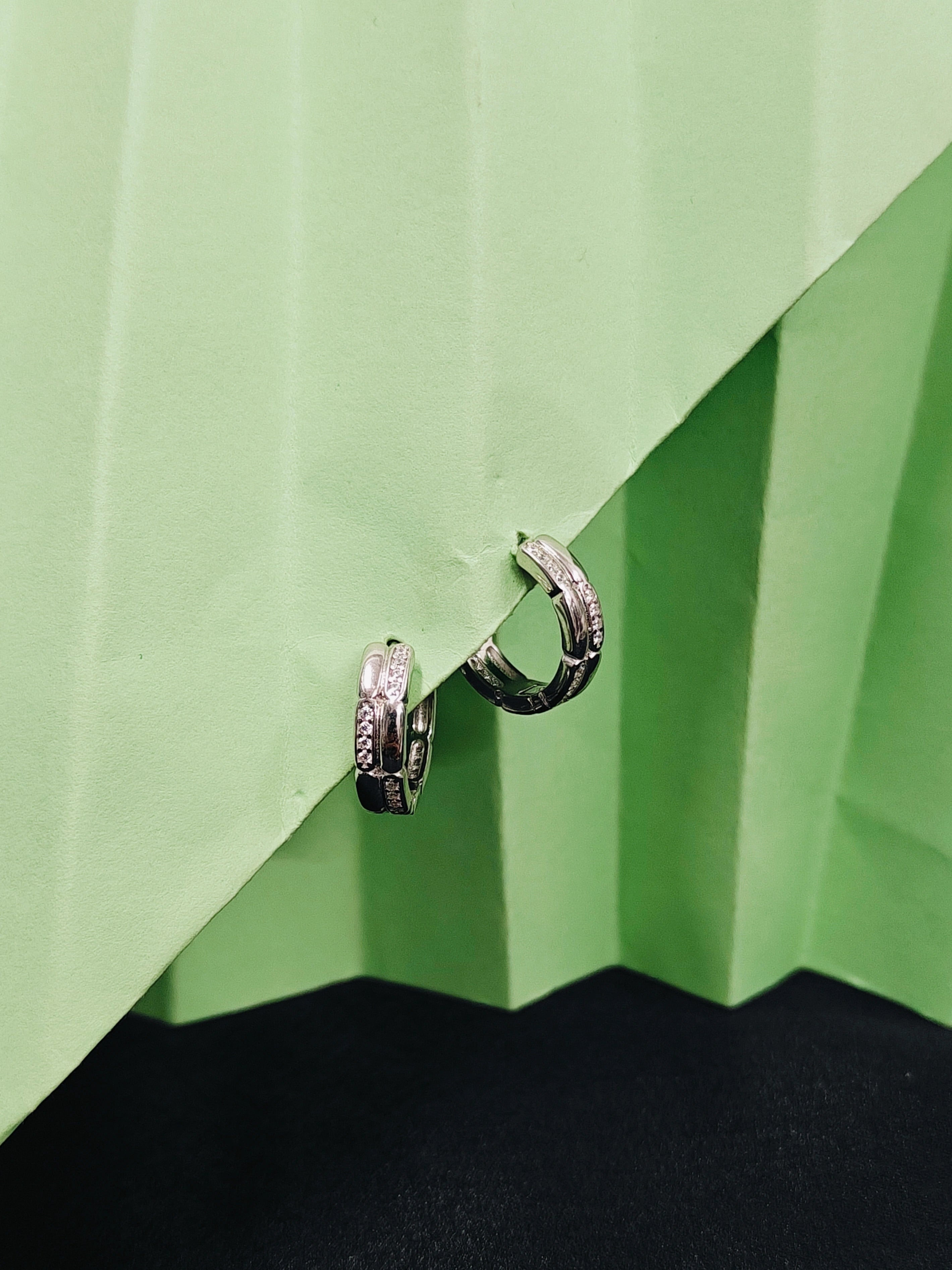 Pair of silver hoop earrings on a green and black geometric background