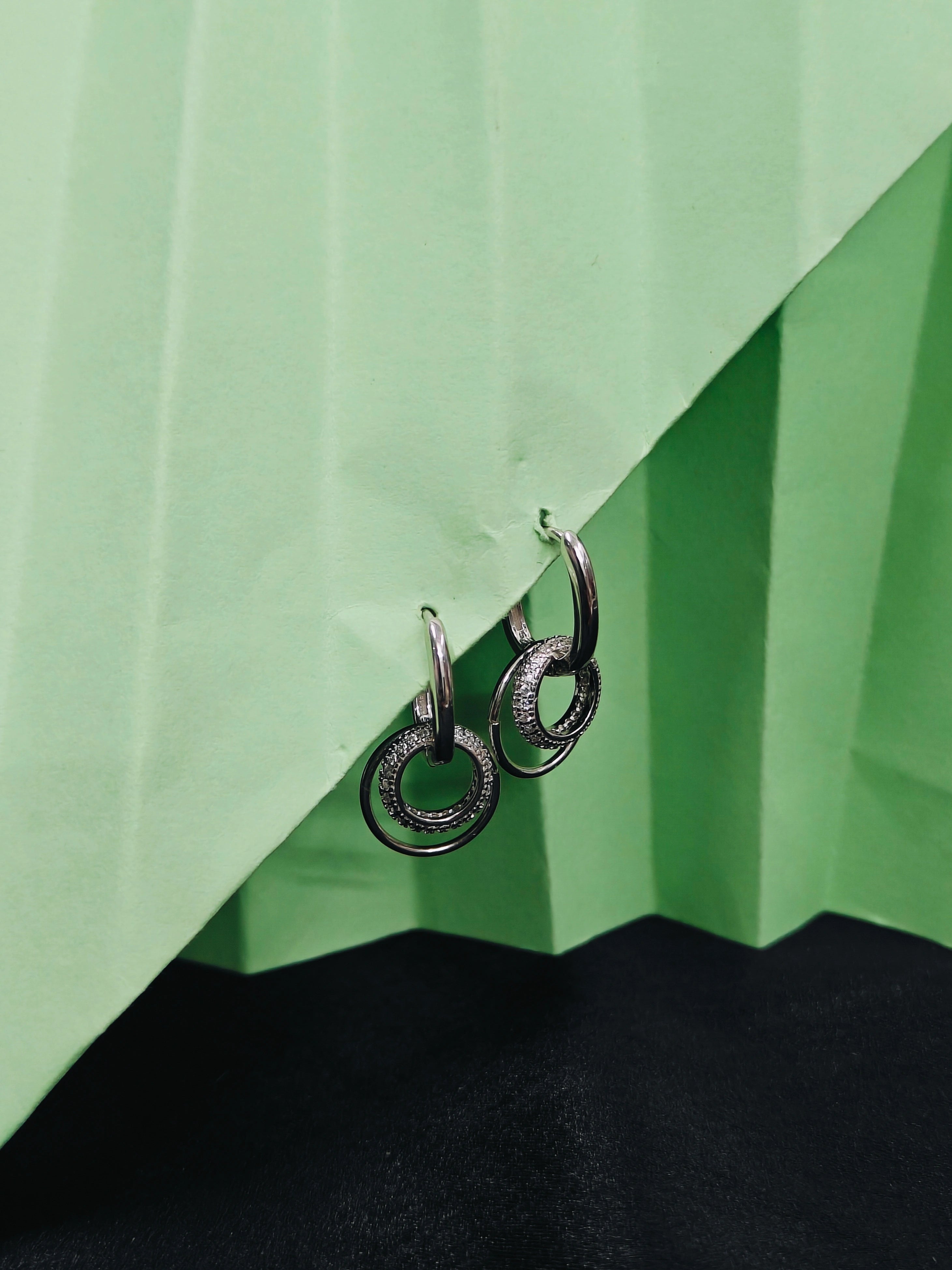 Silver hoop earrings on a green and black geometric background