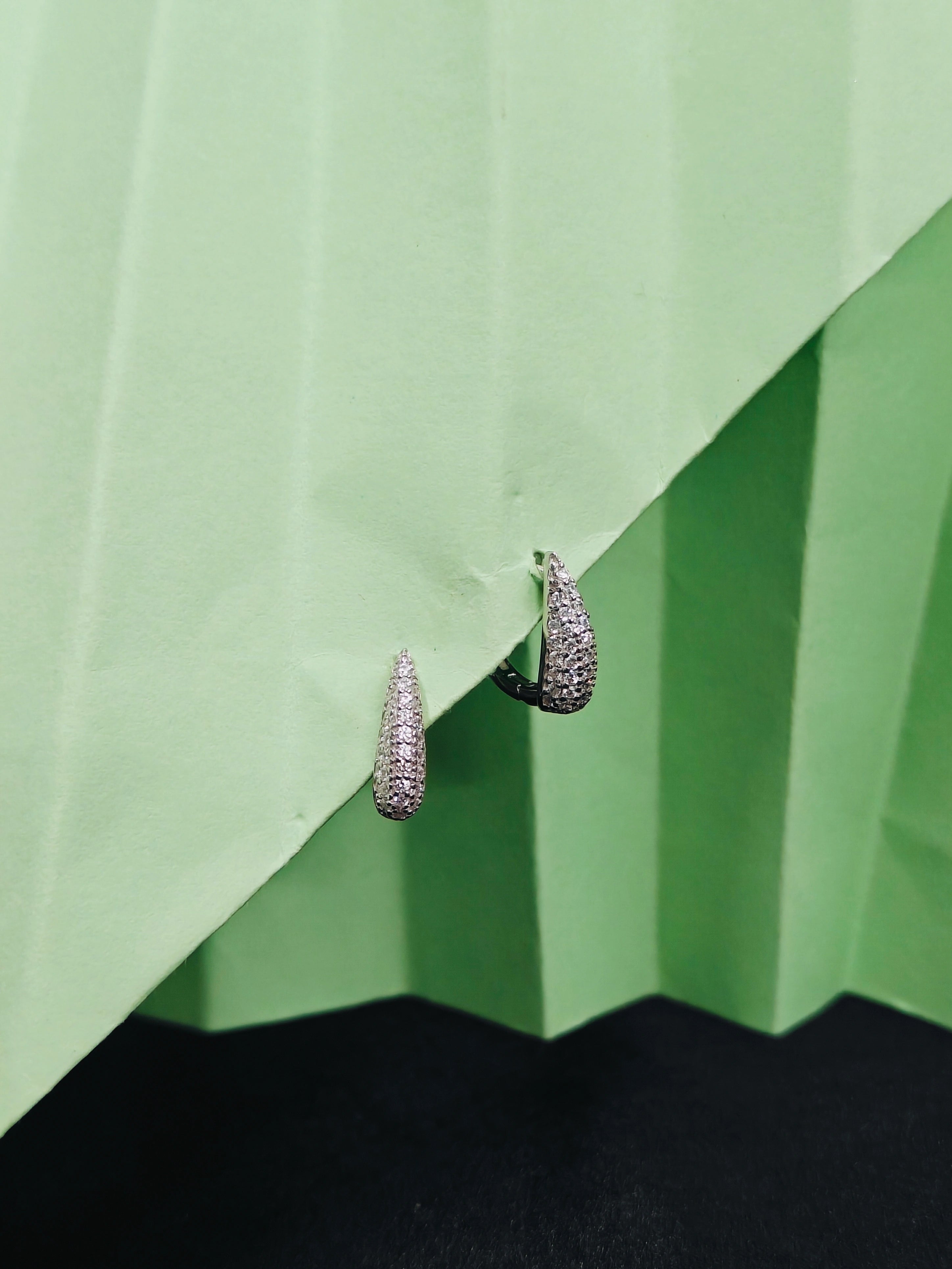 Pair of silver hoop earrings on a green pleated fabric background