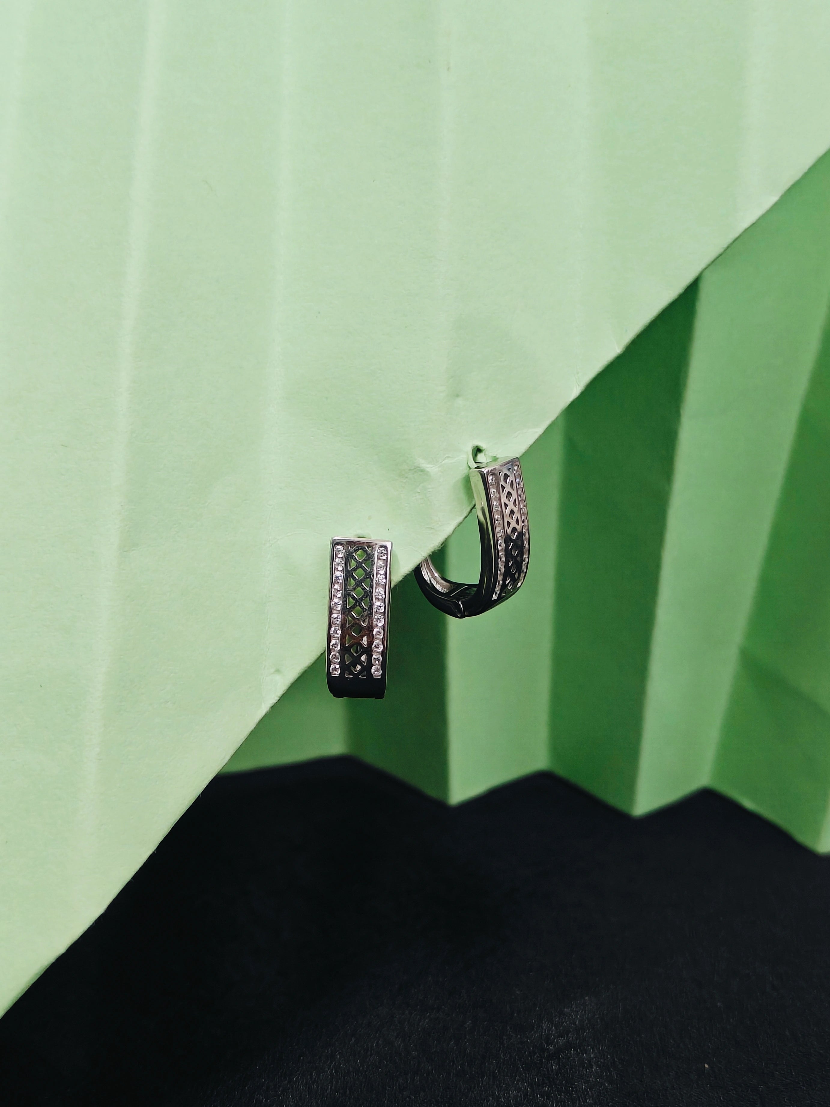 Pair of black hoop earrings on a green and black textured surface