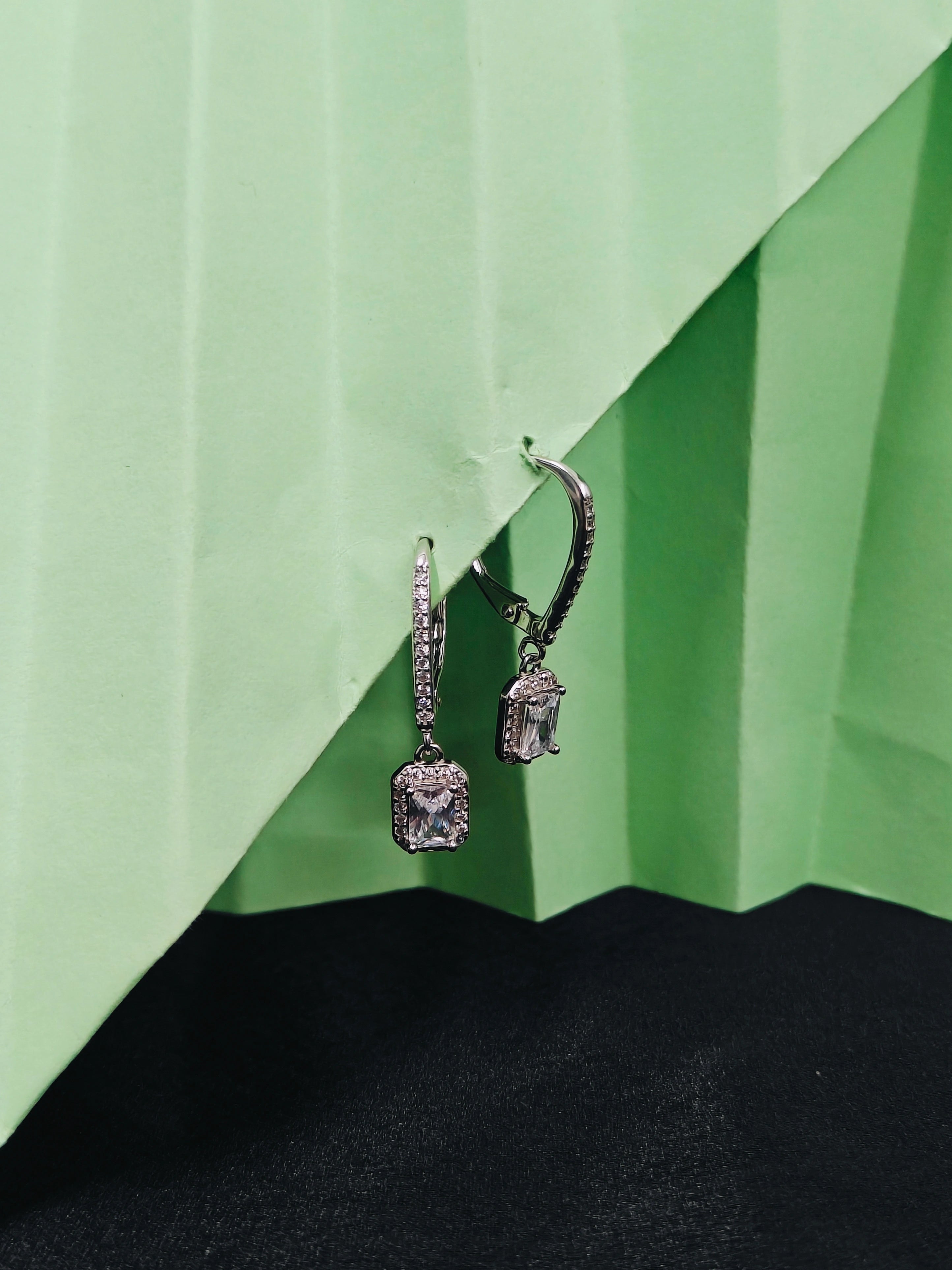 Pair of silver earrings with gemstones on a green and black background
