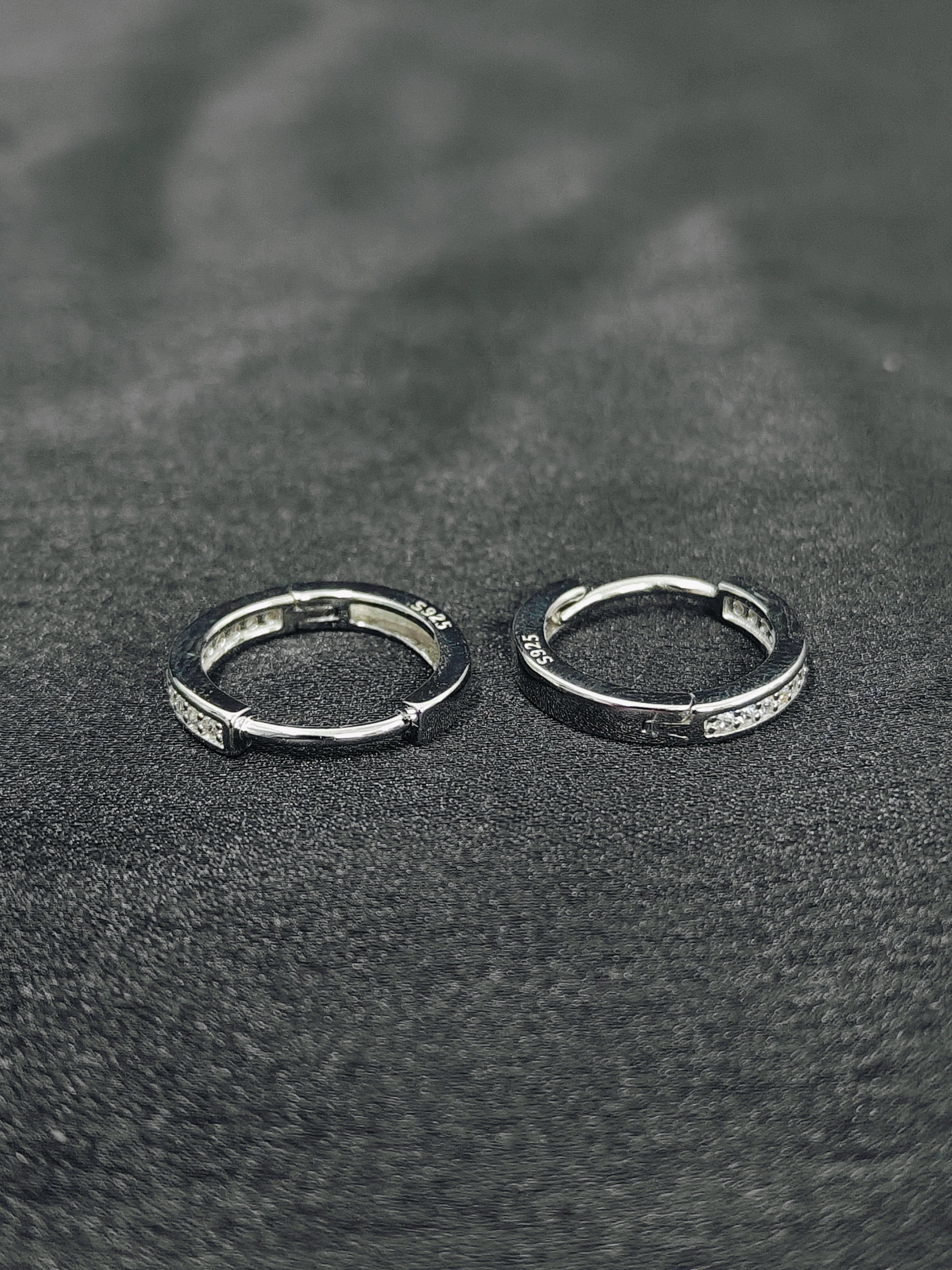 Two silver hoop earrings on a textured black surface