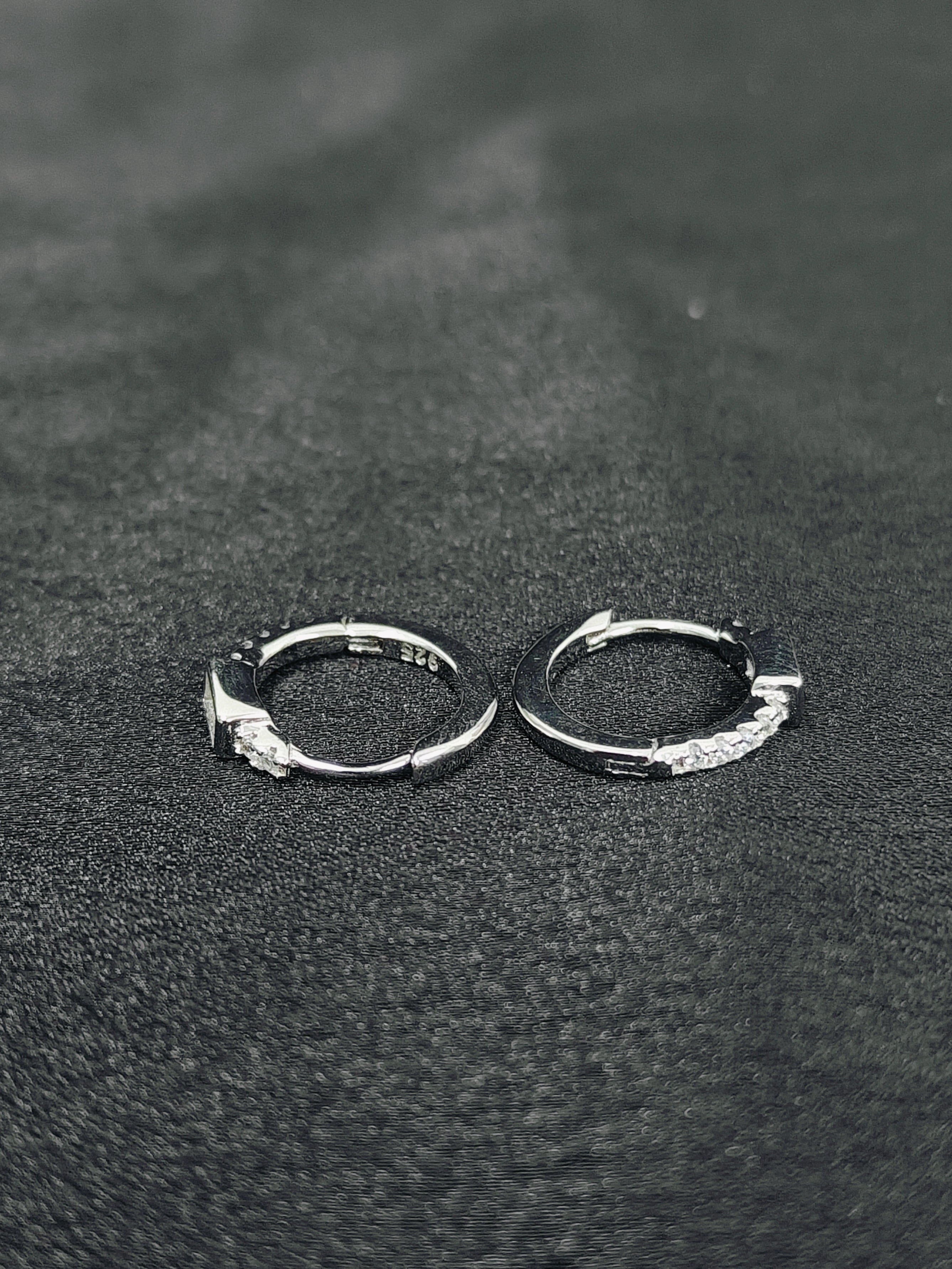 Pair of silver hoop earrings on a textured black surface