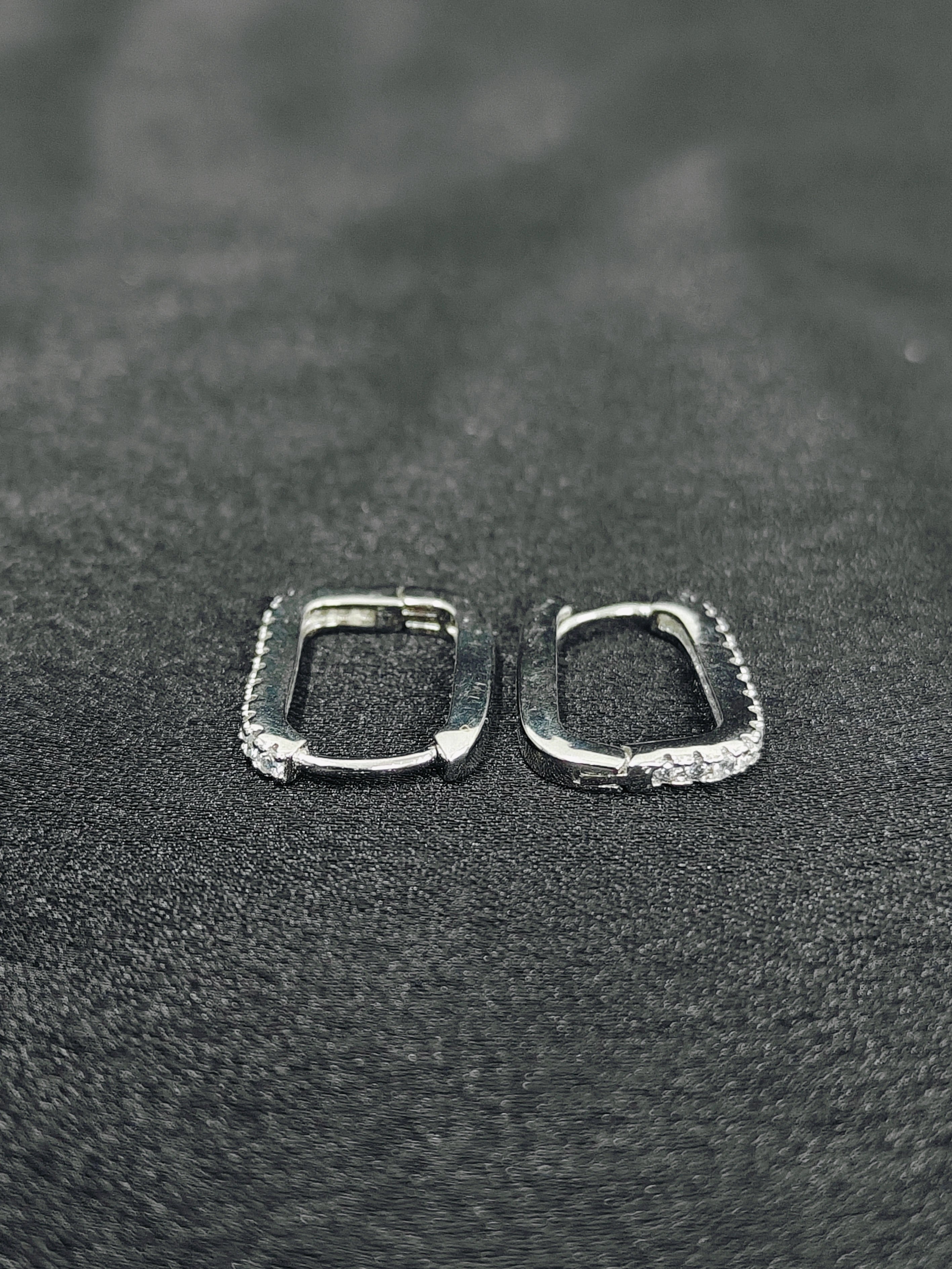 Two silver hoop earrings on a textured black surface