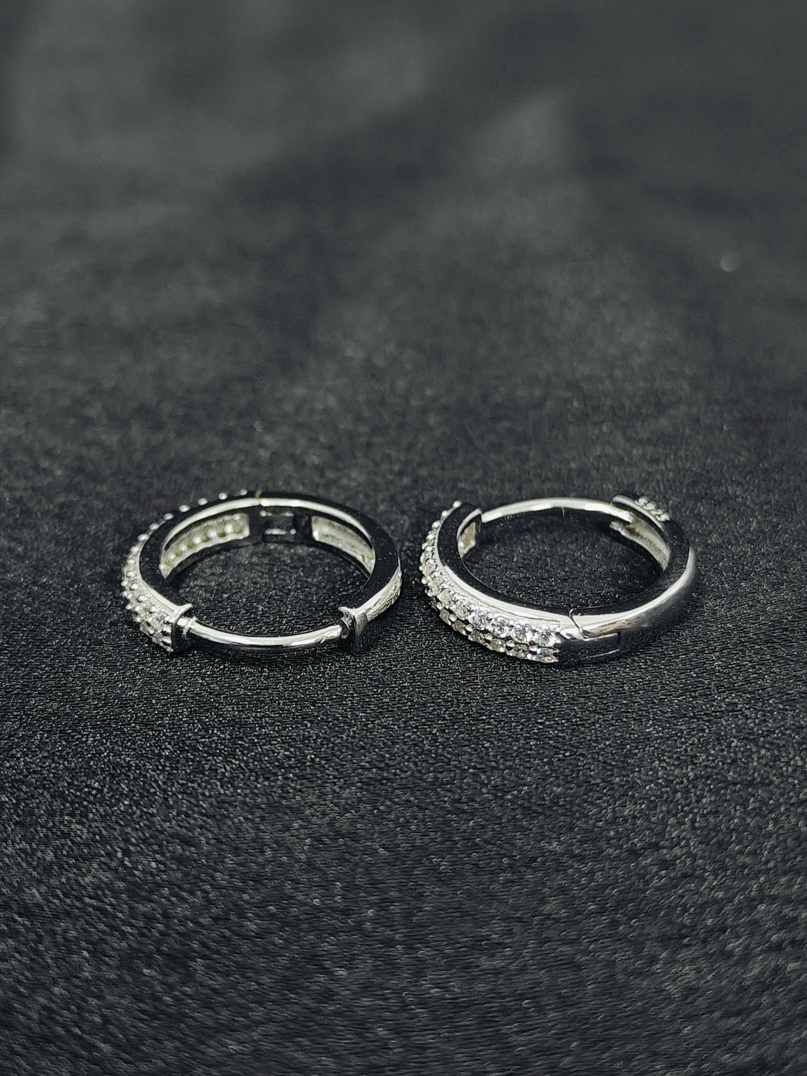 Two silver hoop earrings with embedded stones on a black textured surface