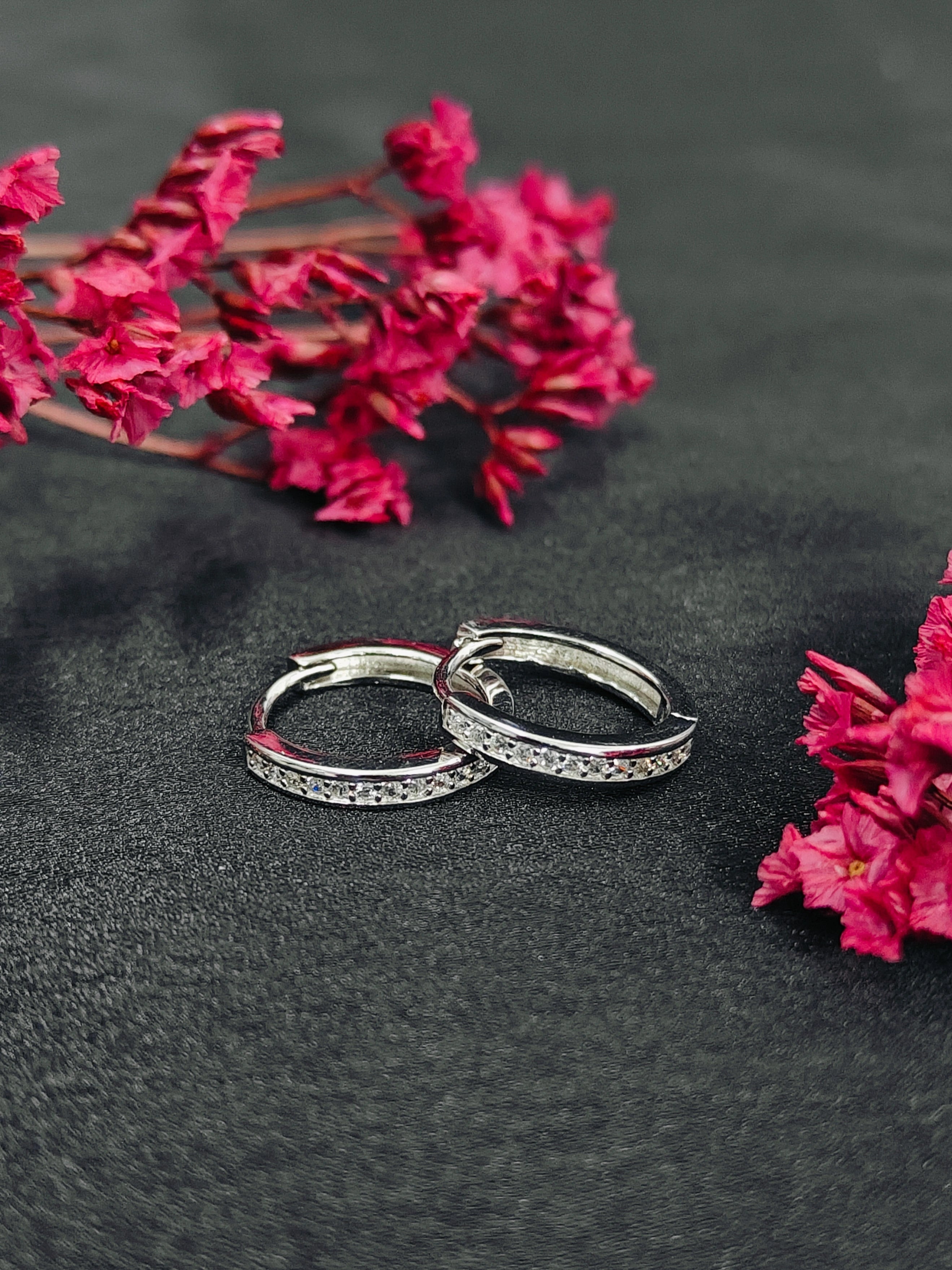 Silver hoop earrings on a dark surface with pink flowers.