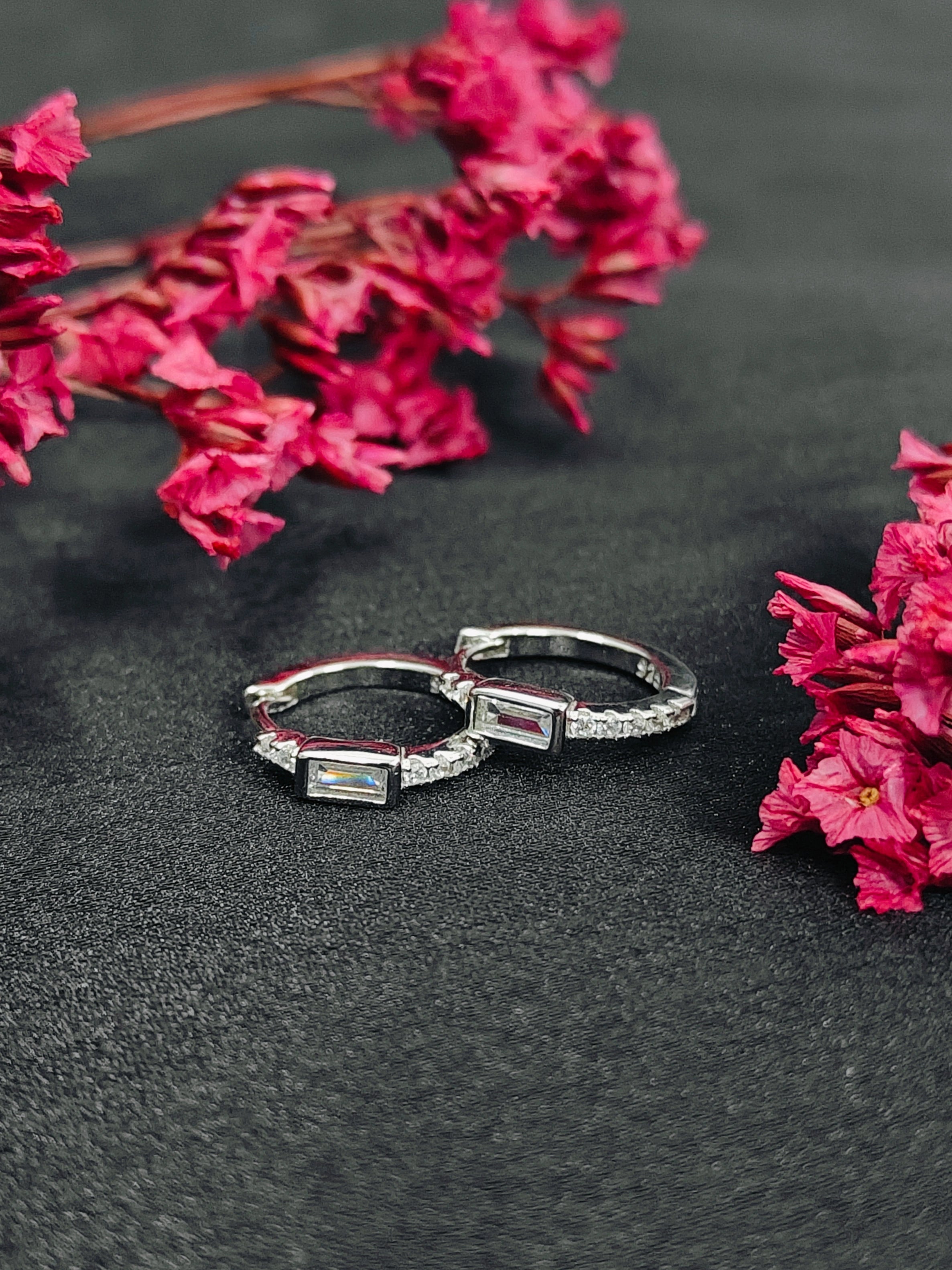 Two silver rings with gemstones on a dark surface with pink flowers.