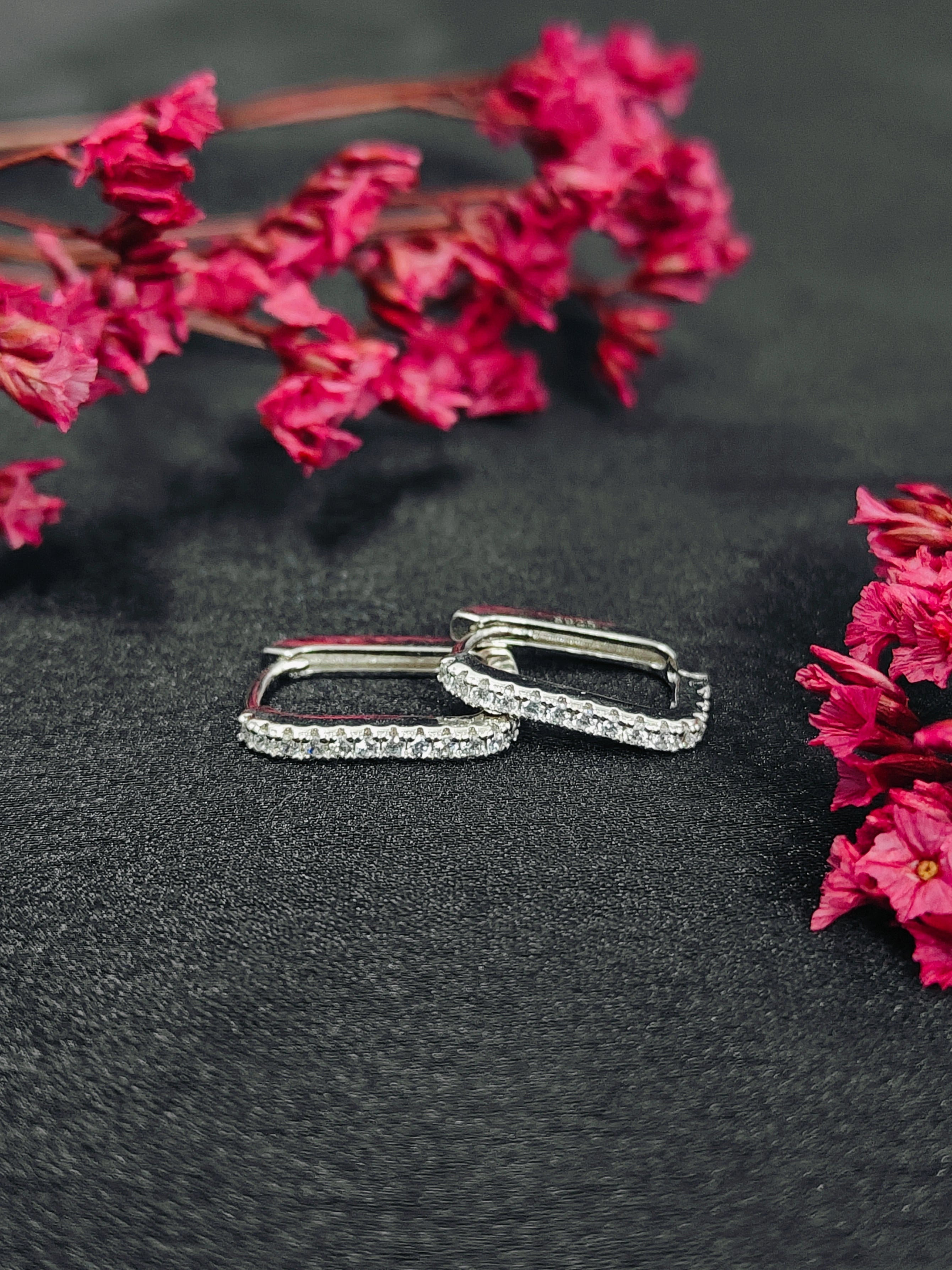 Silver hoop earrings on a dark surface with pink flowers