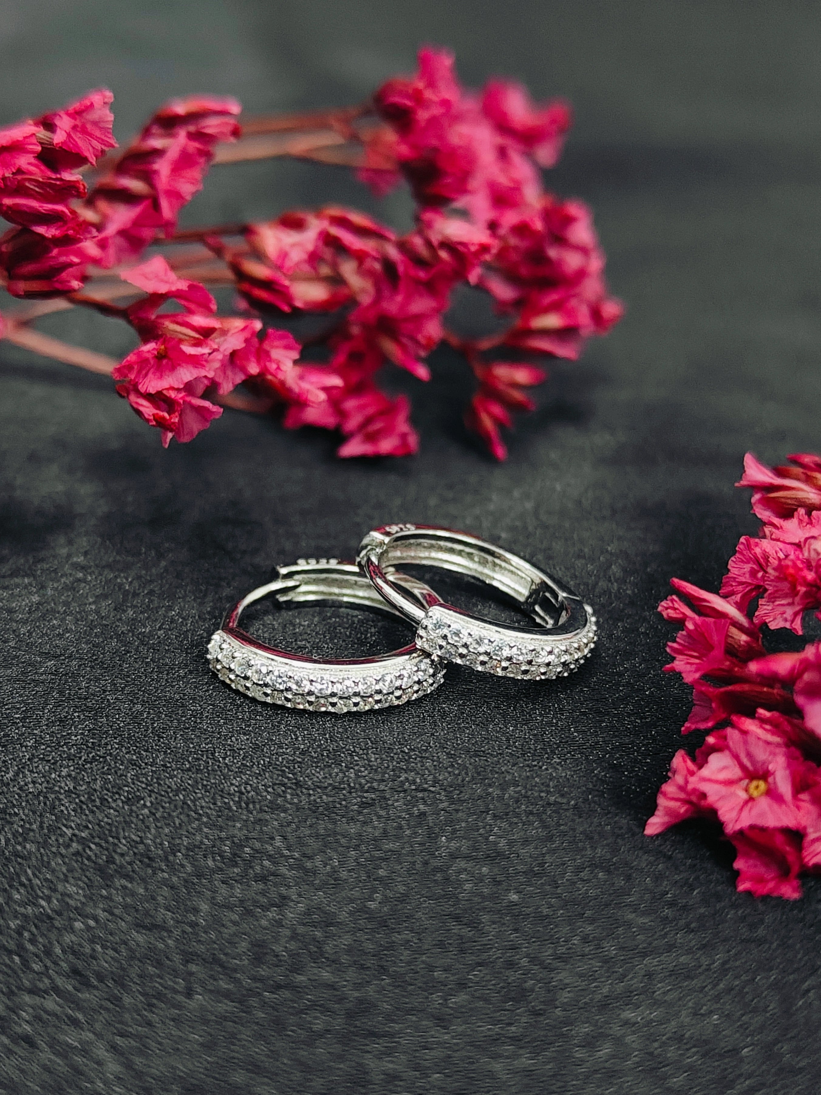 Silver hoop earrings with embedded stones on a dark surface with pink flowers.