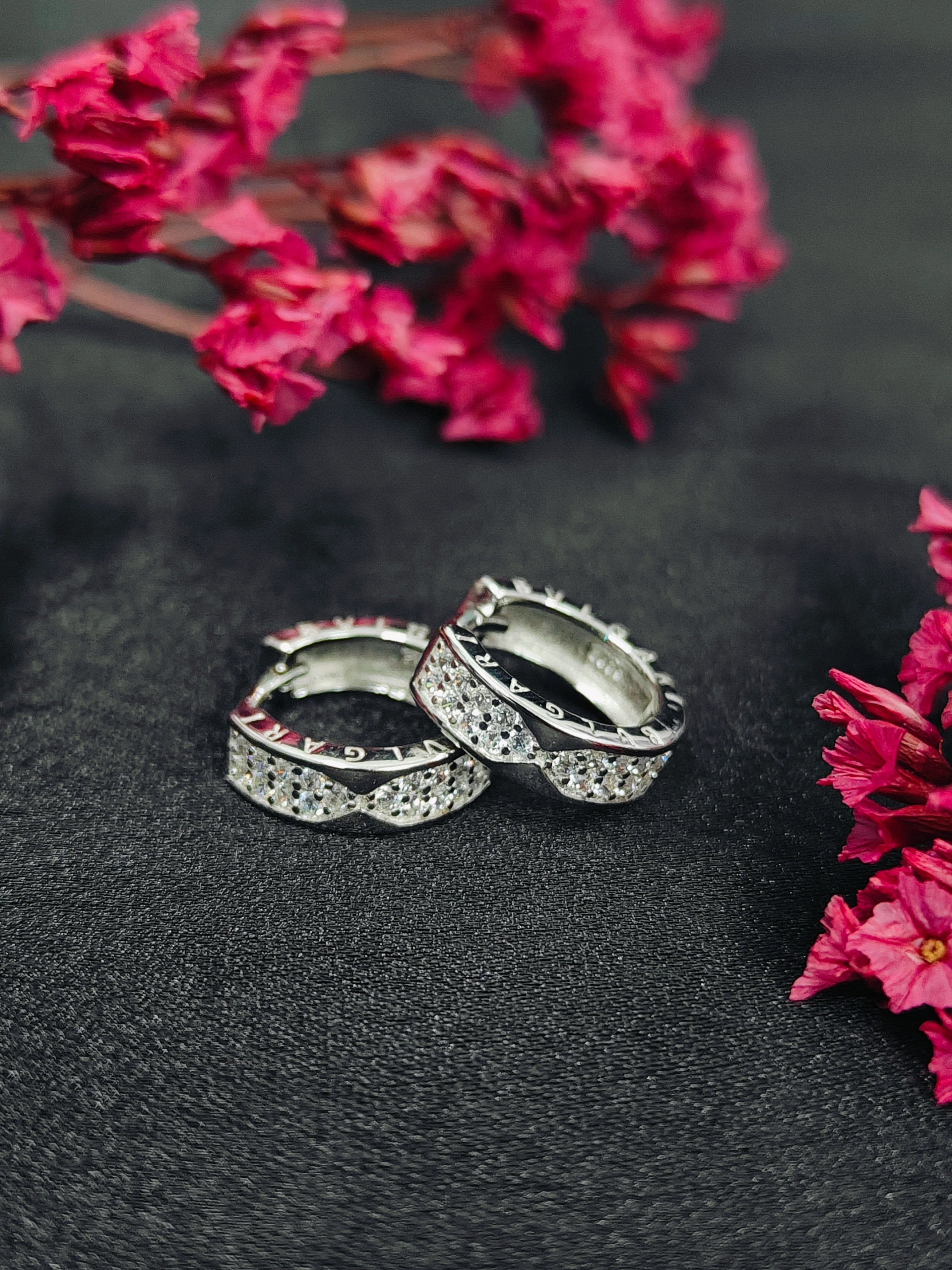 Silver hoop earrings with gemstones on a dark surface with pink flowers.