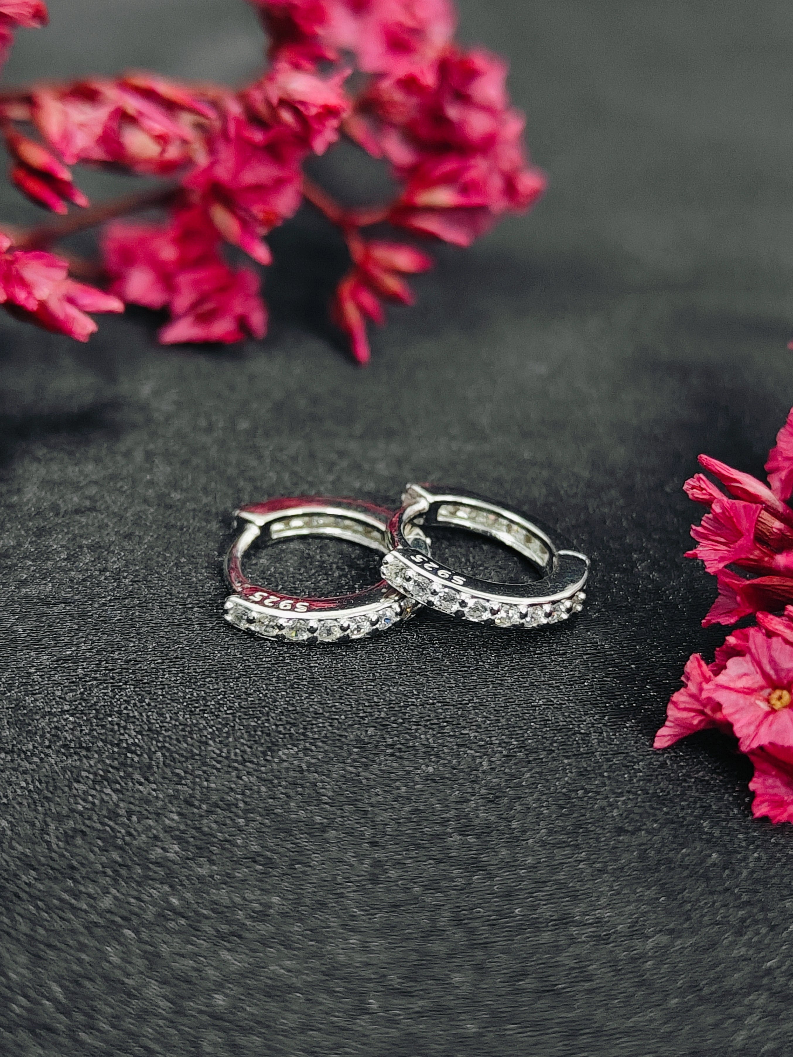 Silver hoop earrings on a dark surface with pink flowers