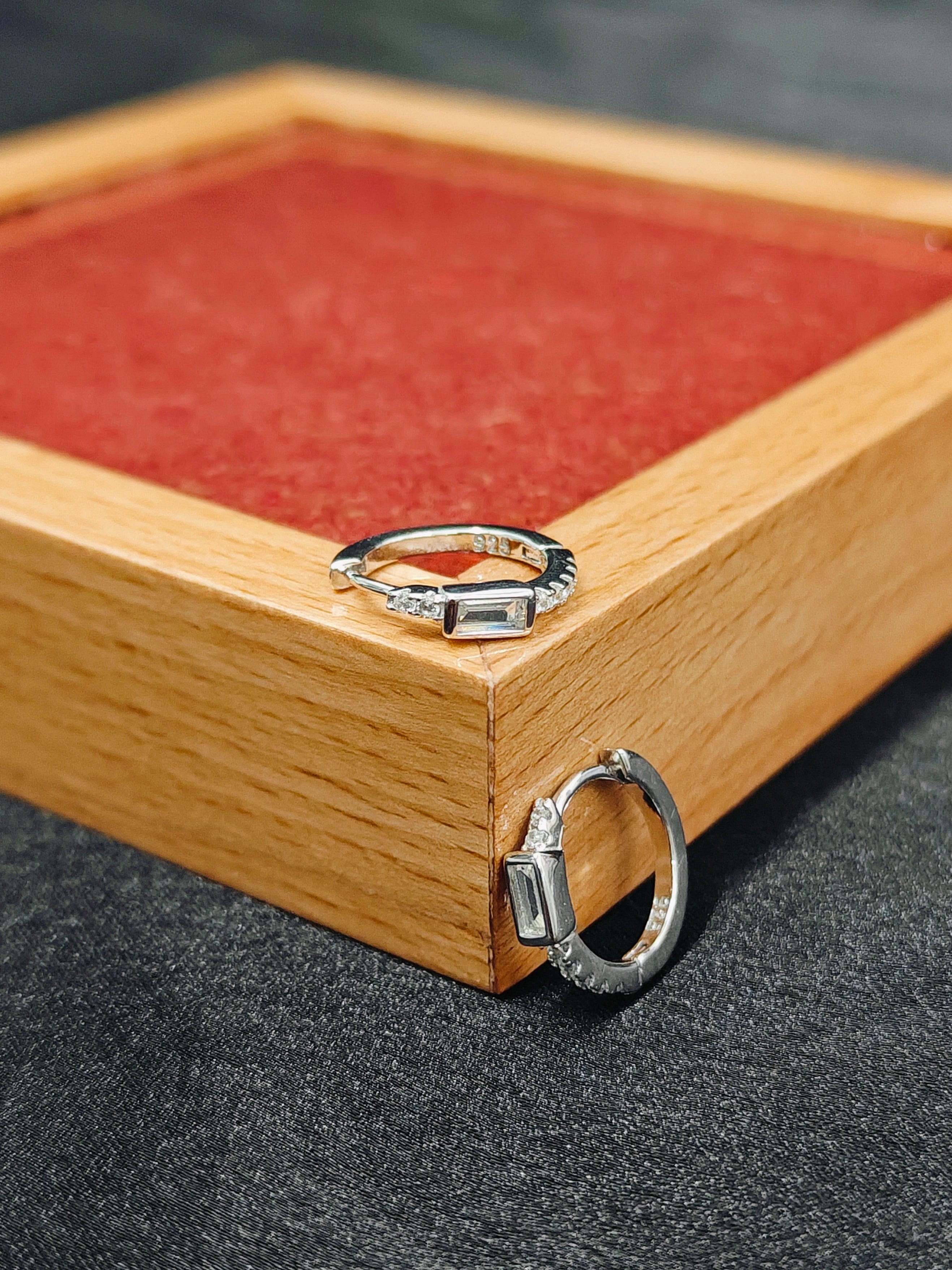 Two silver rings on a wooden box with red interior