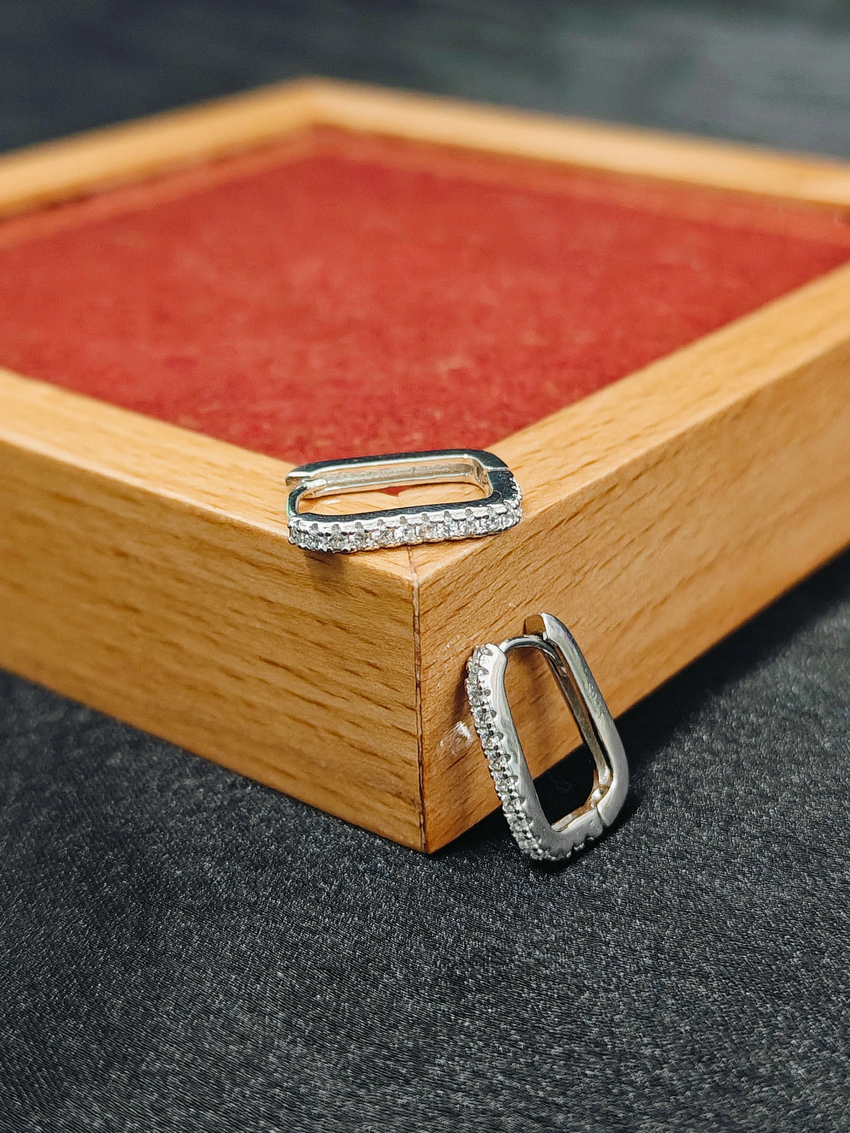 Silver hoop earrings on a wooden jewelry box with a red interior.