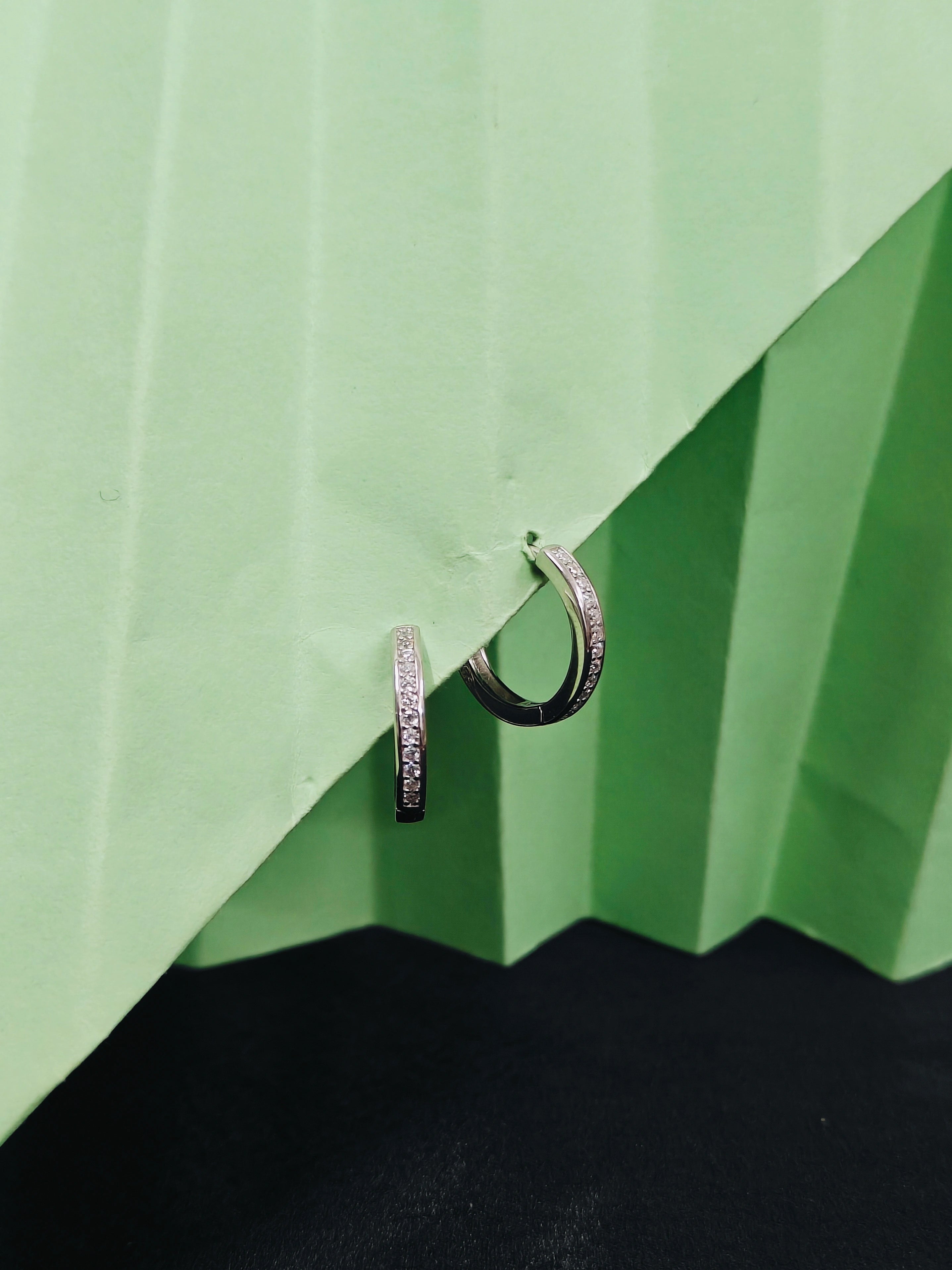 Two silver hoop earrings on a green and black striped background