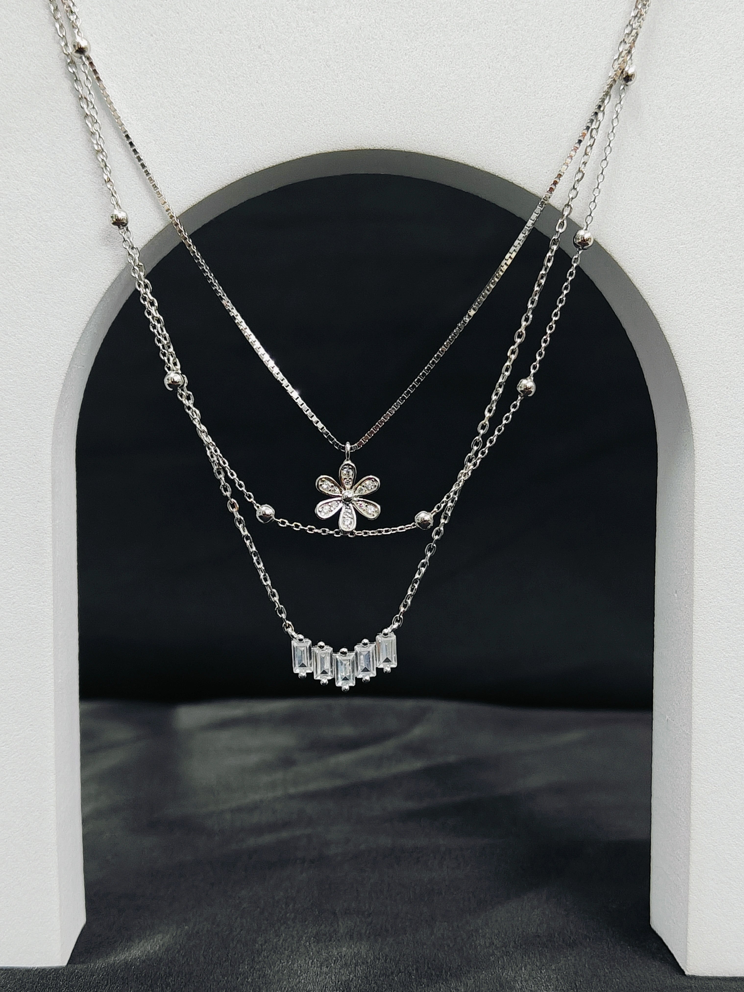 Layered silver necklaces with floral and bar pendants on a dark background
