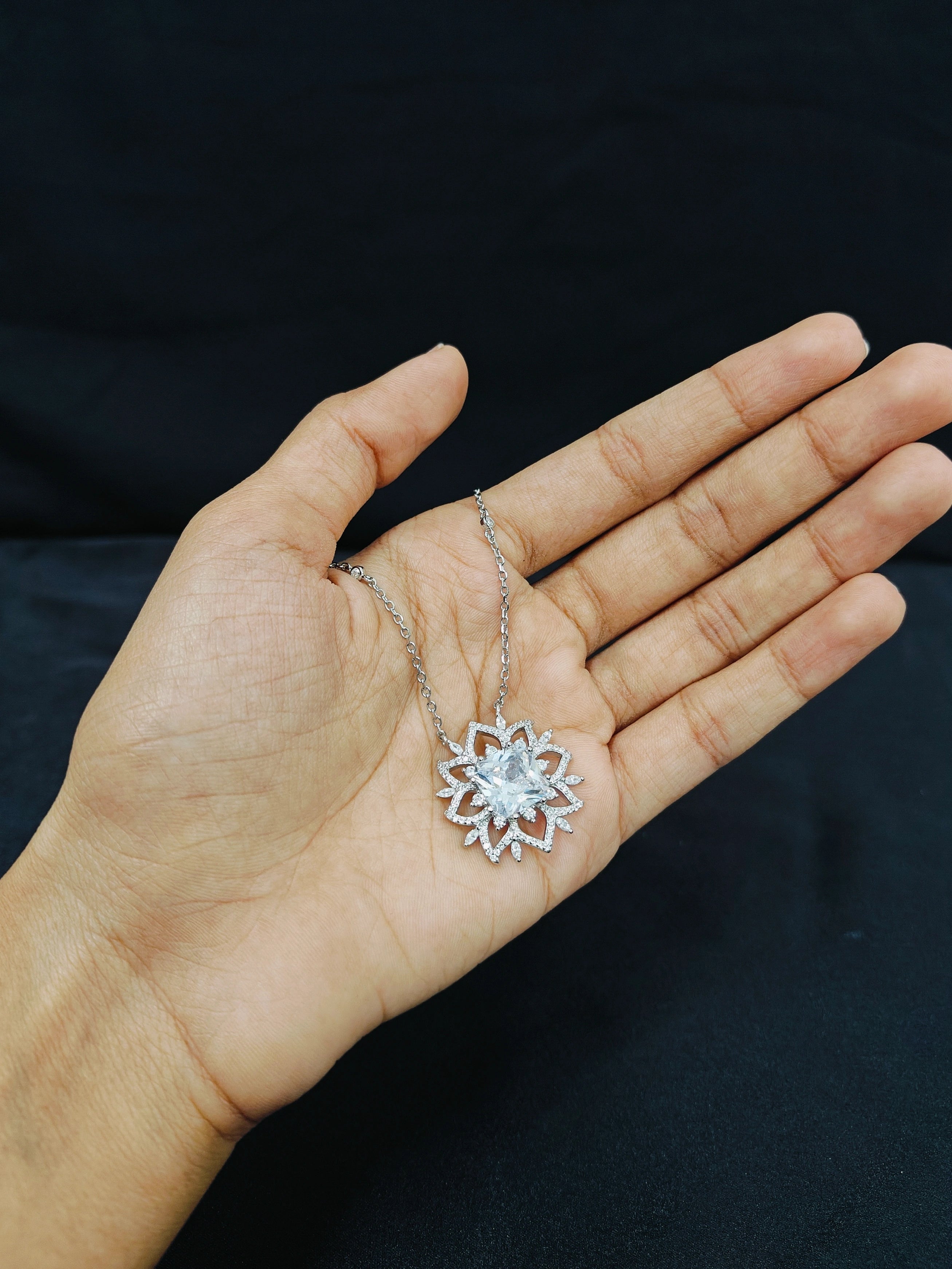 Hand holding a silver necklace with a snowflake pendant against a dark background