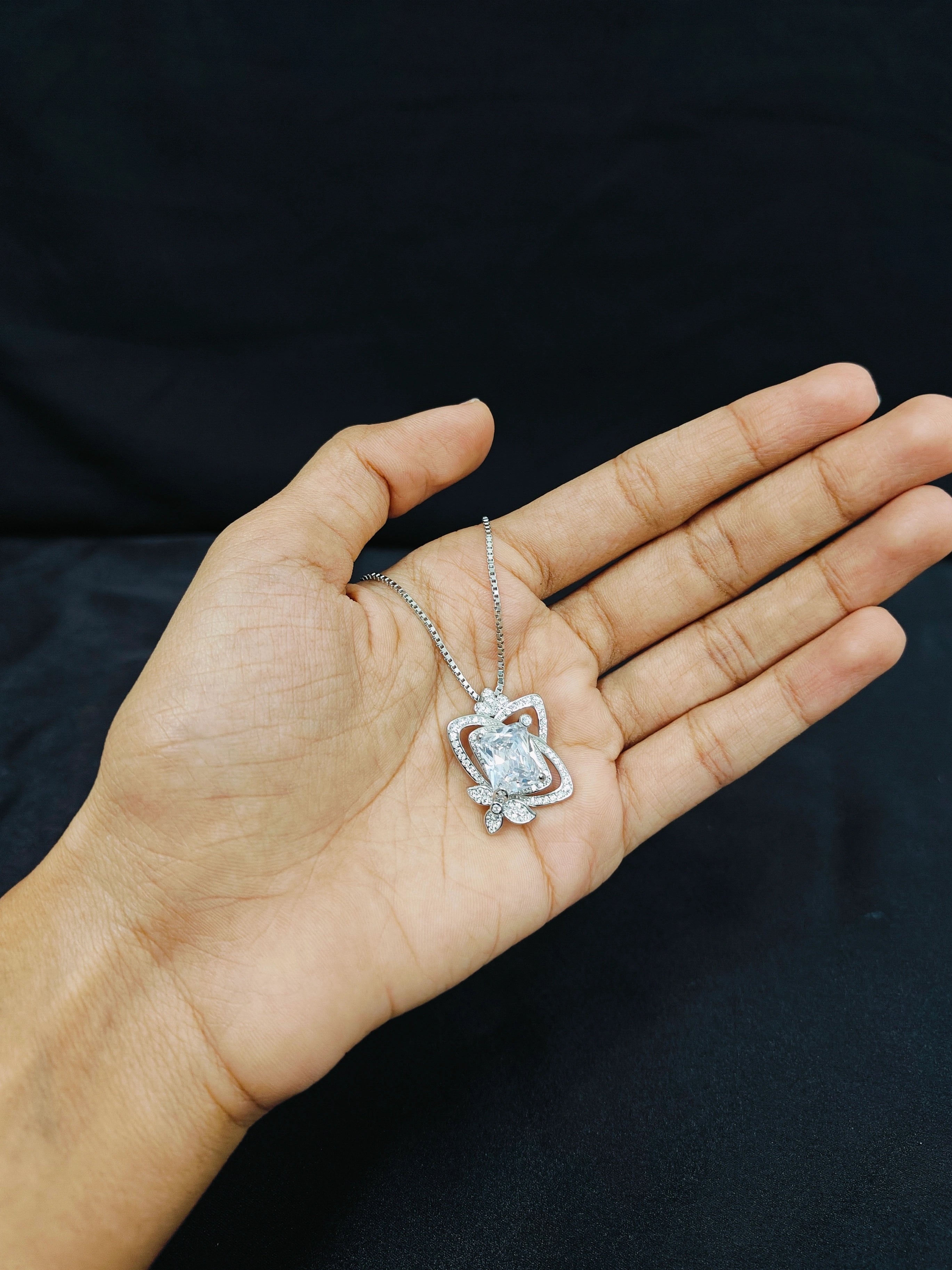 Hand holding a silver necklace with a diamond pendant against a black background