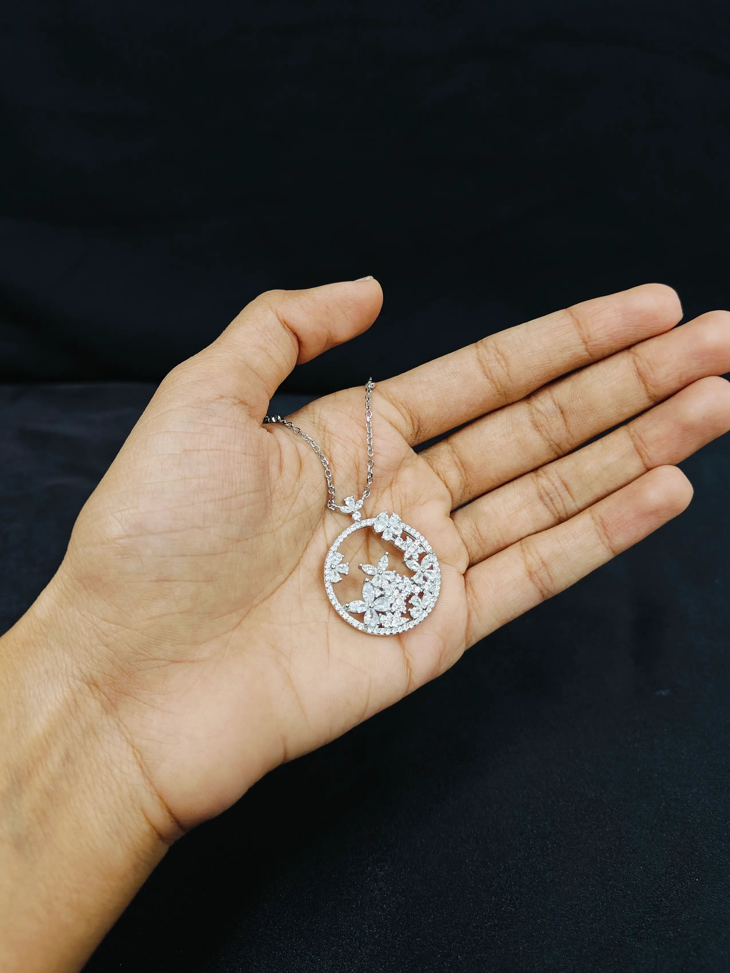 Hand holding a silver necklace with a star and moon pendant against a black background