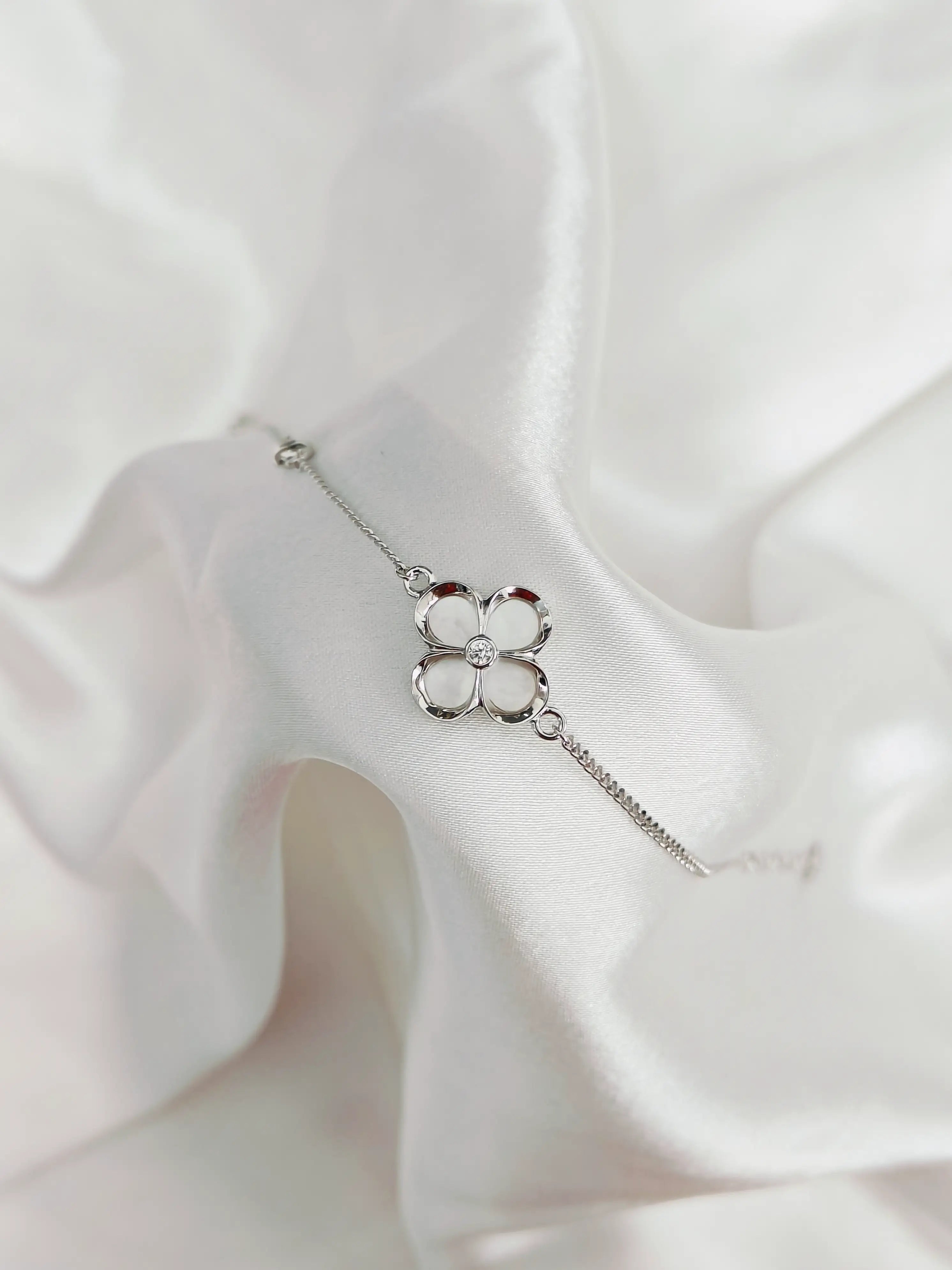 Silver bracelet with clover design on a white fabric background