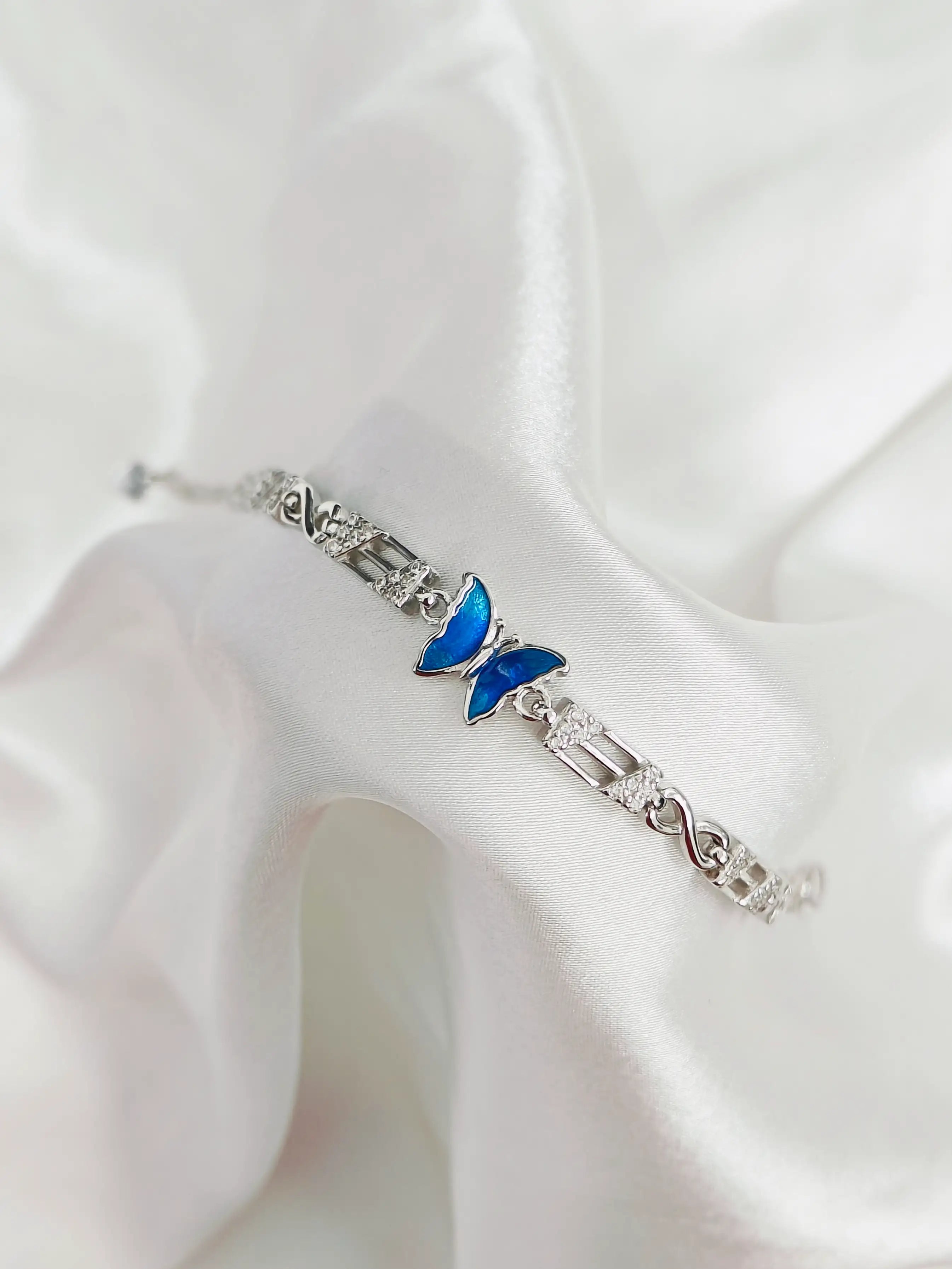 Silver bracelet with a blue butterfly charm on a white fabric background