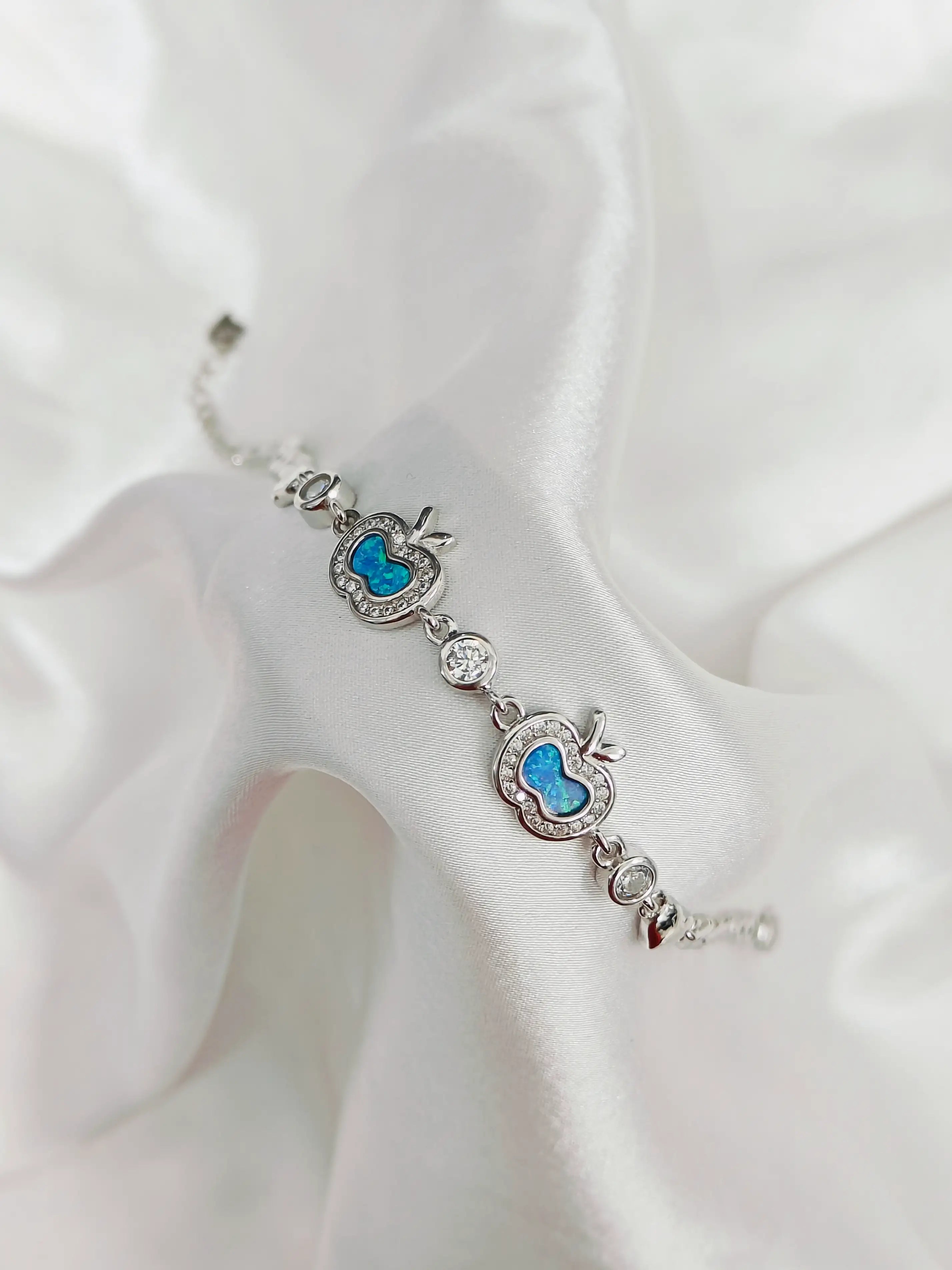 Silver bracelet with blue heart charms on a white fabric background
