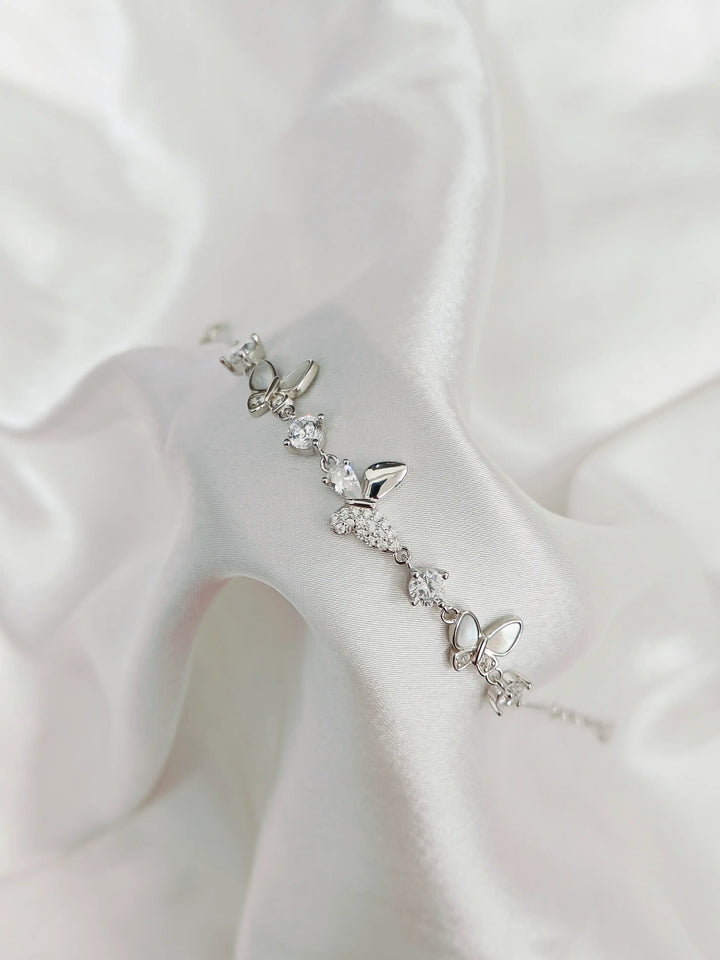 Silver bracelet with butterfly charms on a white fabric background