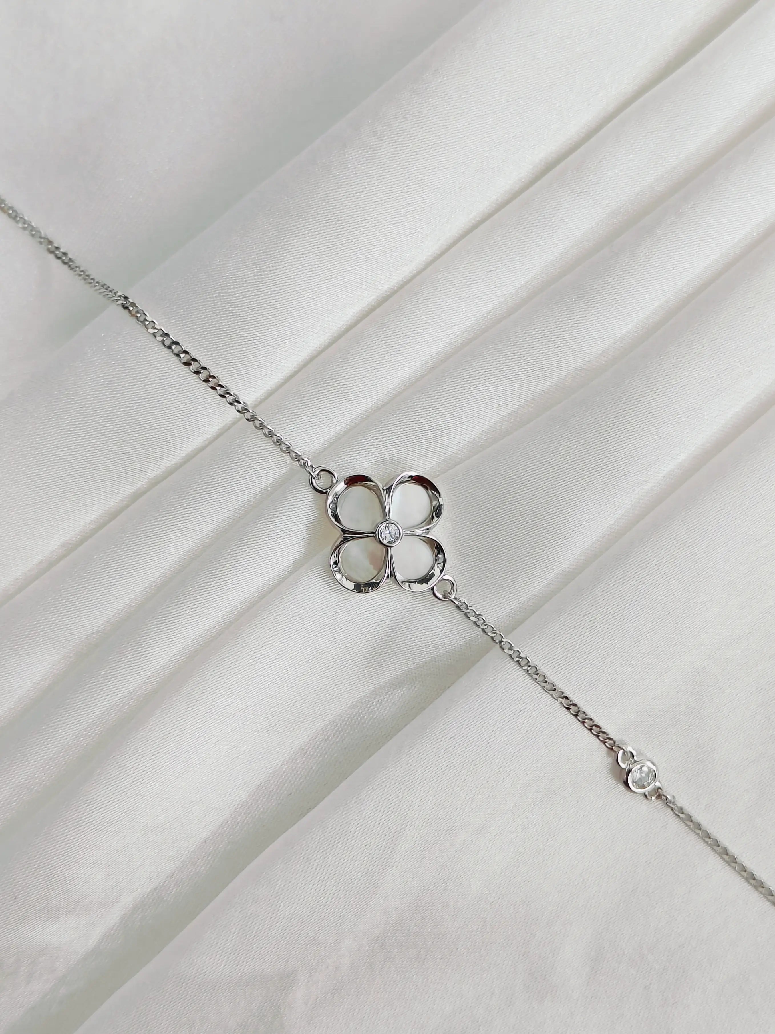 Silver bracelet with a clover-shaped charm on a white fabric background