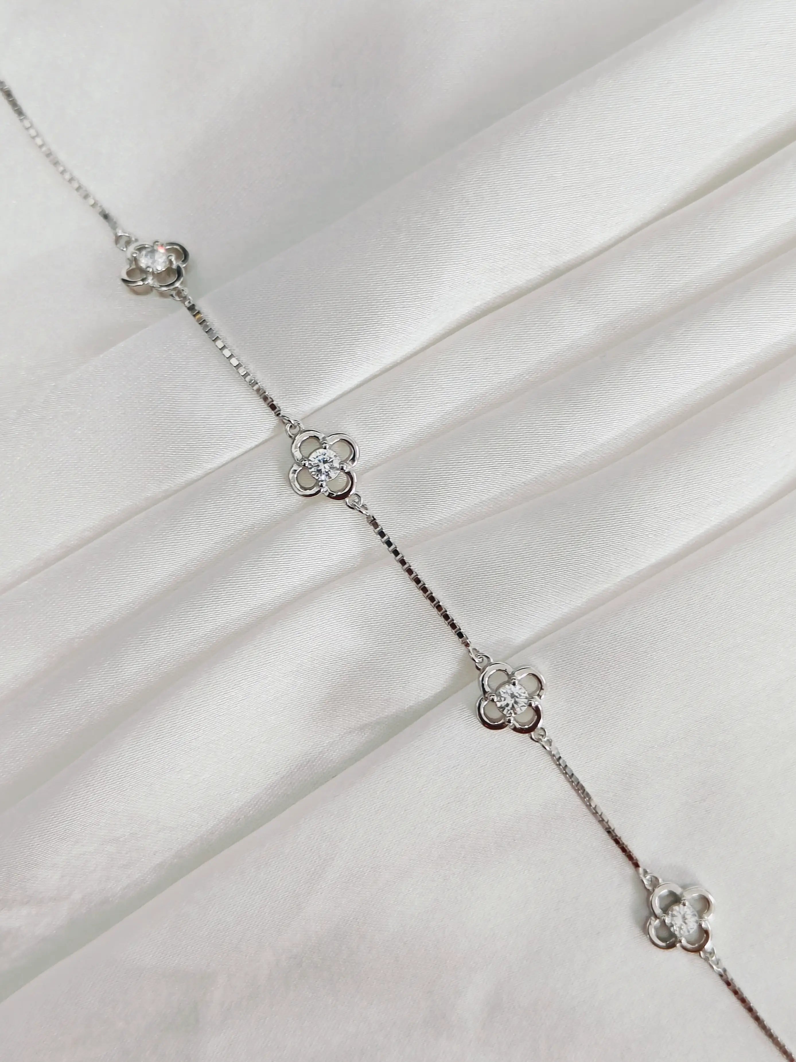 Silver necklace with floral designs on a white fabric background