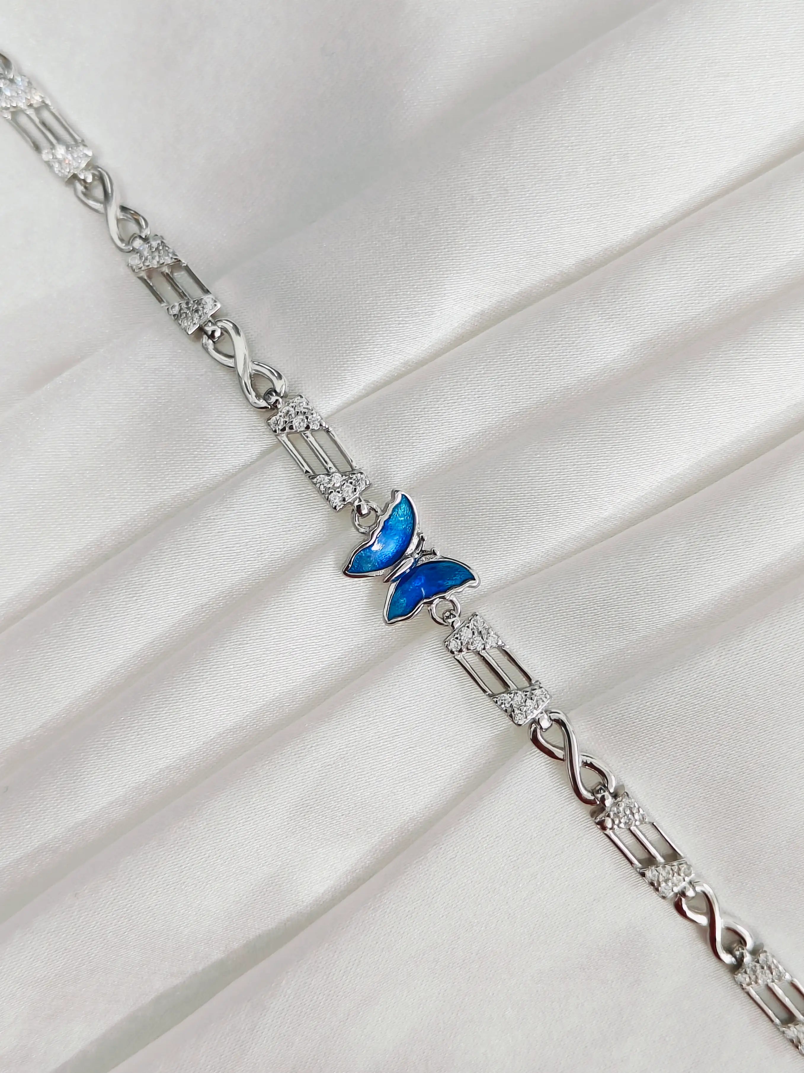 Silver bracelet with a blue butterfly charm on a white fabric background