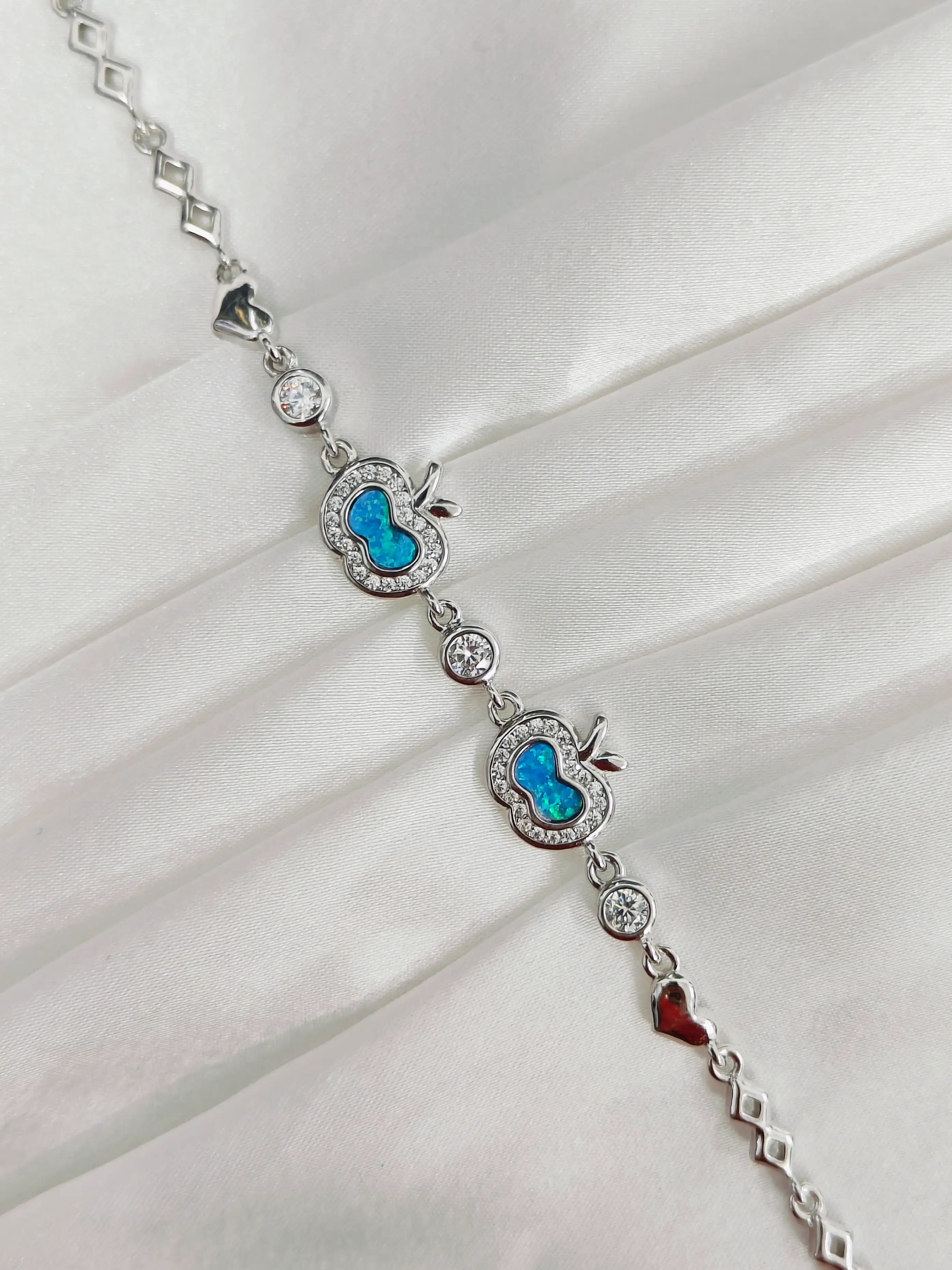 Silver bracelet with blue heart charms and a red heart charm on a white fabric background