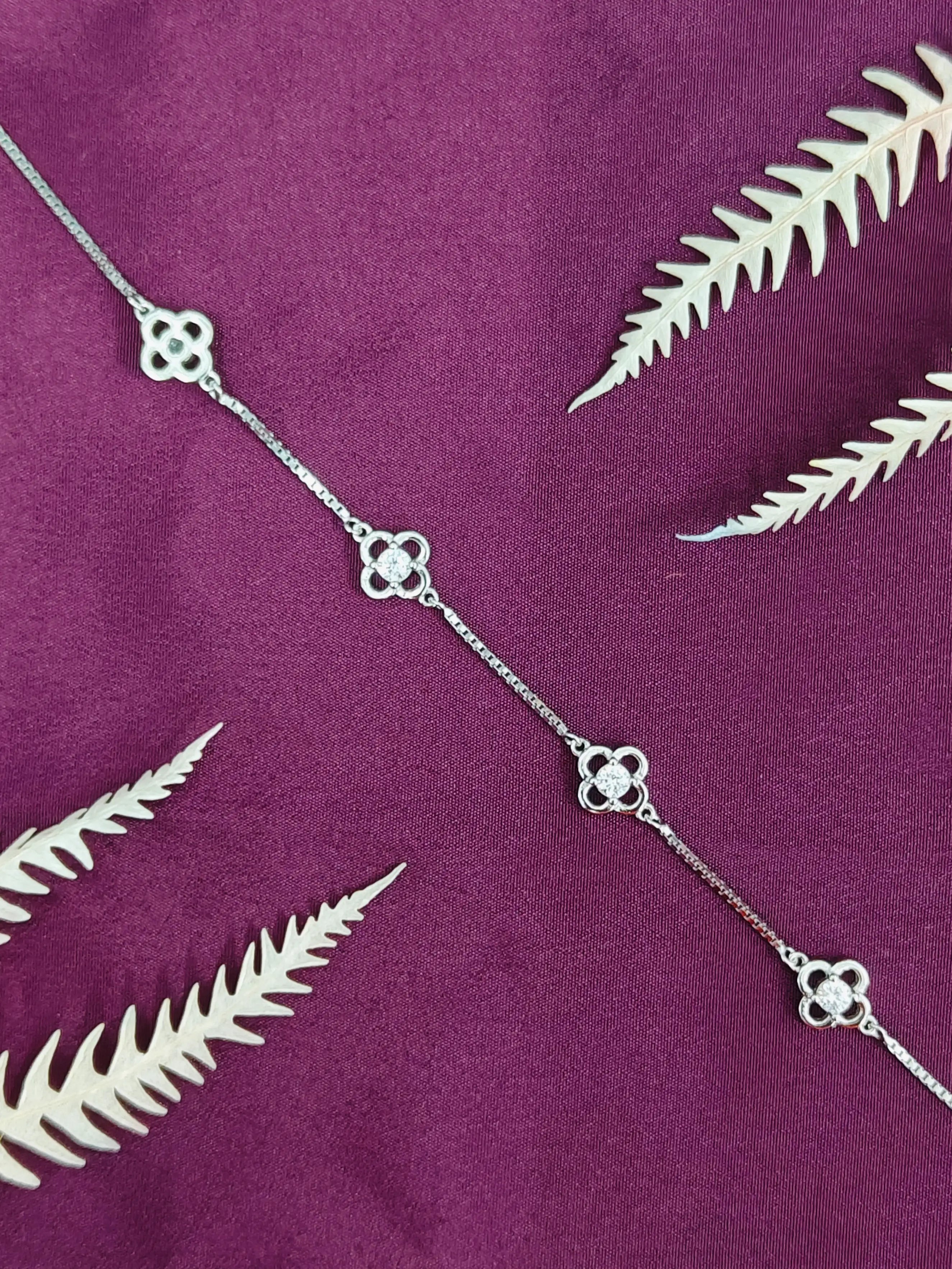 Silver necklace with leaf-like pendants on a purple fabric background