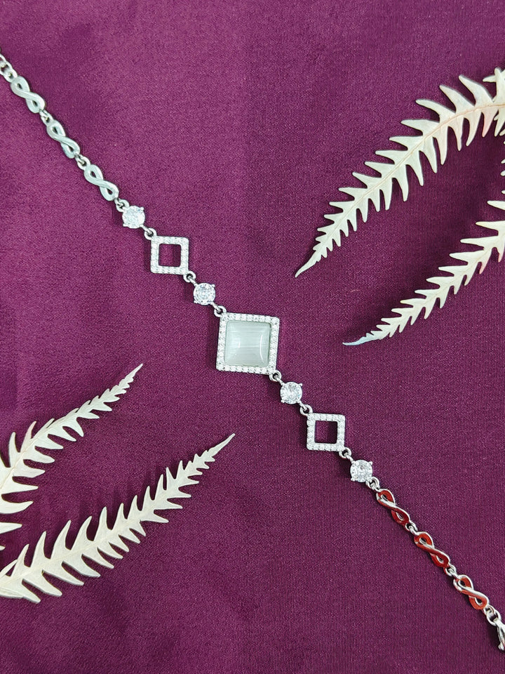 Silver necklace with diamond-like stones on a purple fabric background with leaf patterns