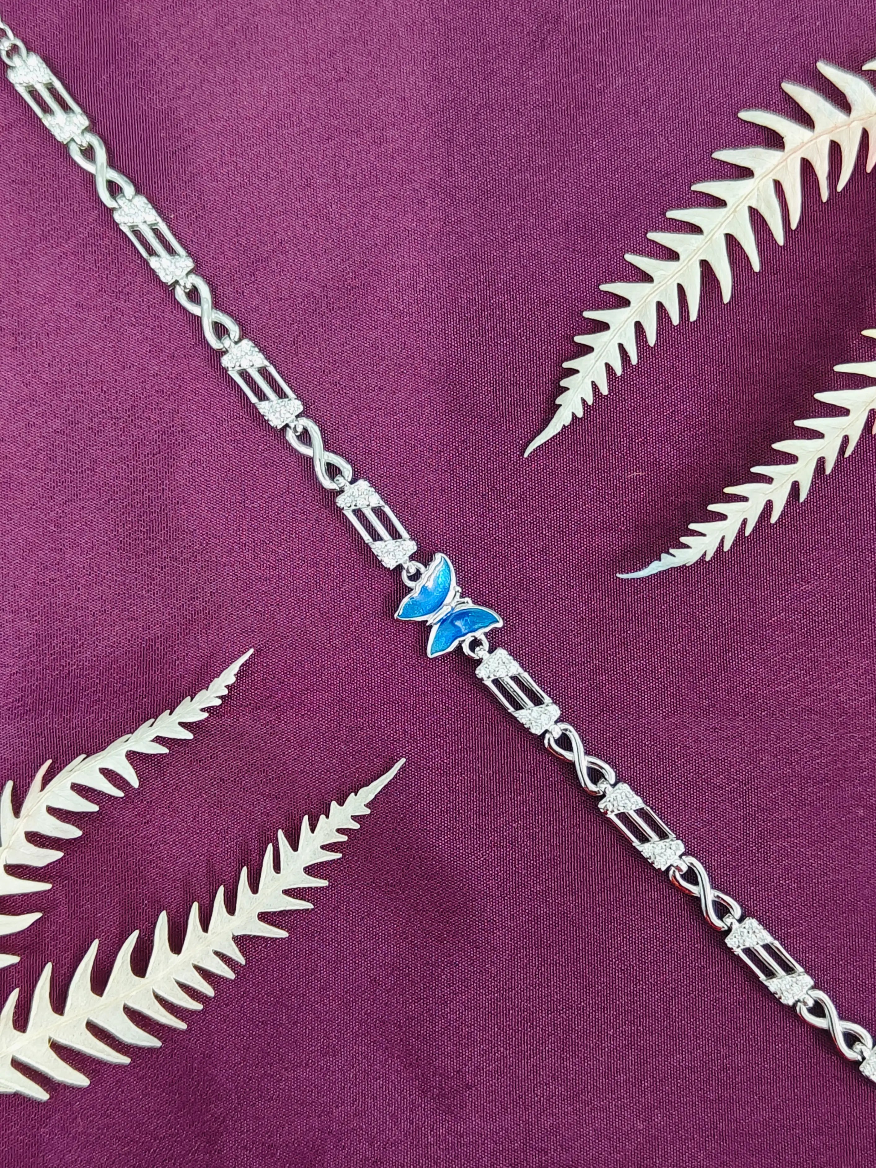 Silver bracelet with a blue butterfly charm on a purple fabric background with white leaf patterns.