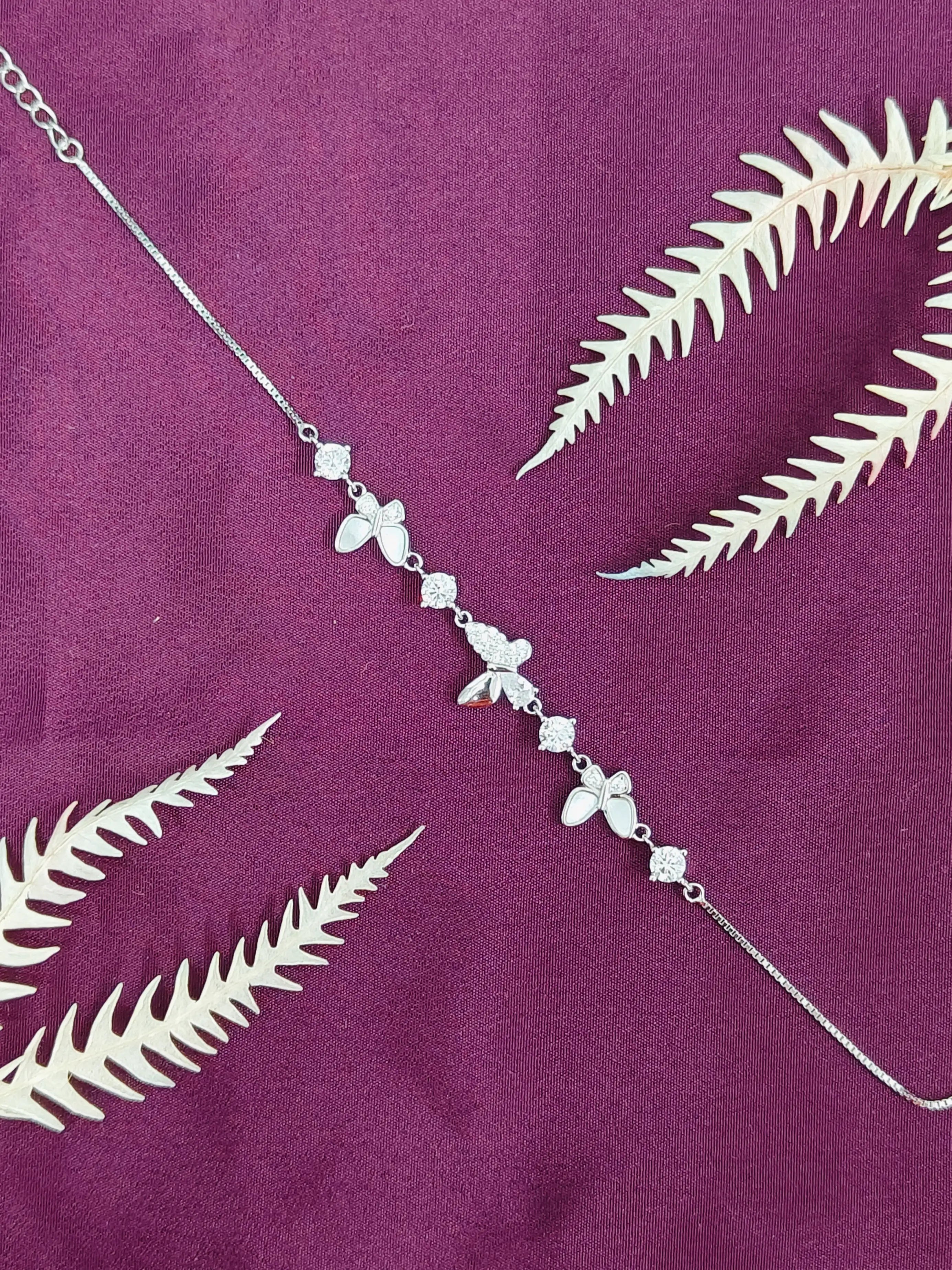 Silver leaf-shaped necklace on a purple fabric background with white leaves.