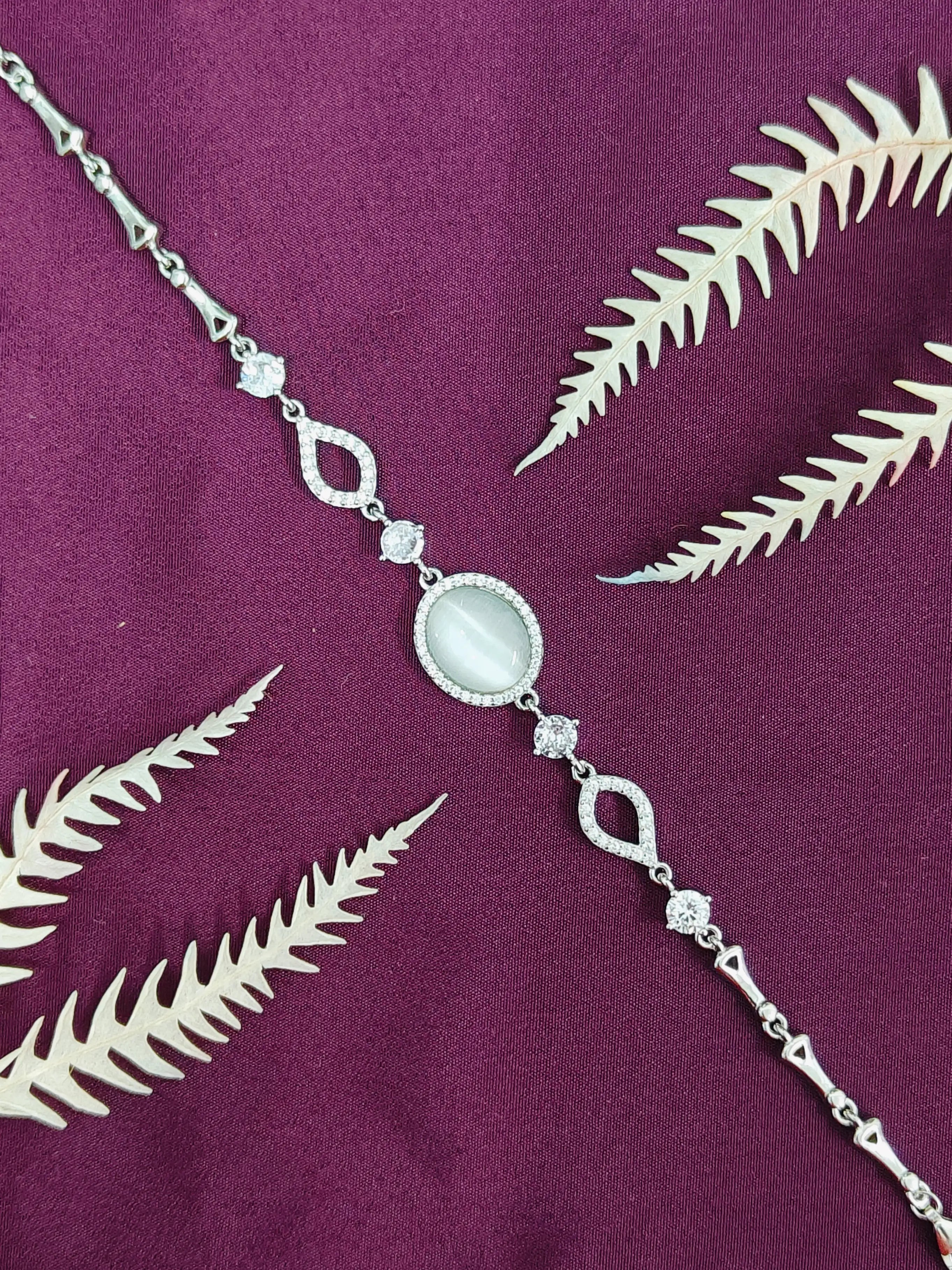 Silver necklace with a central gemstone on a purple fabric background with leaf patterns