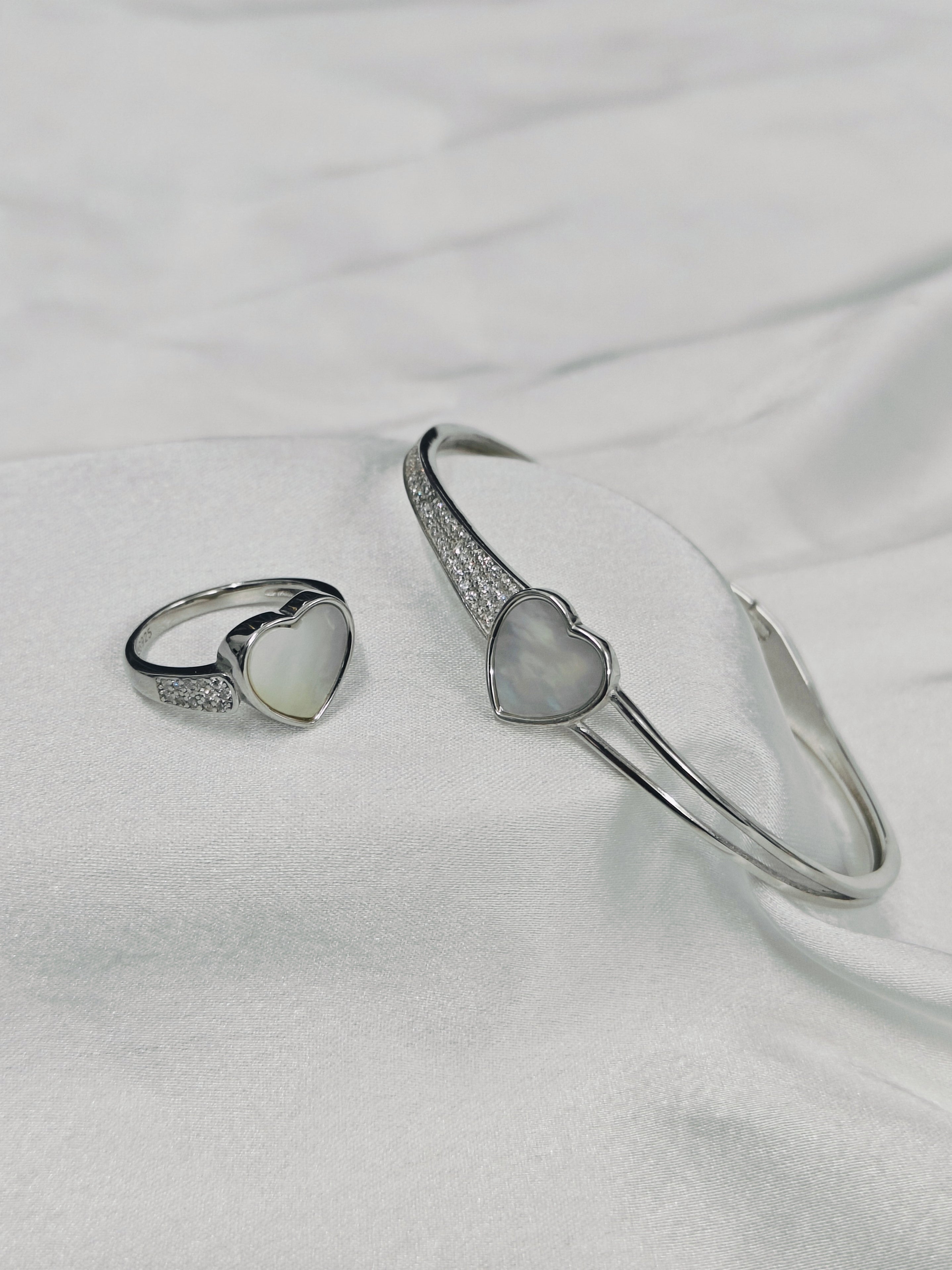 Silver bracelet and ring with heart-shaped stones on a white fabric background