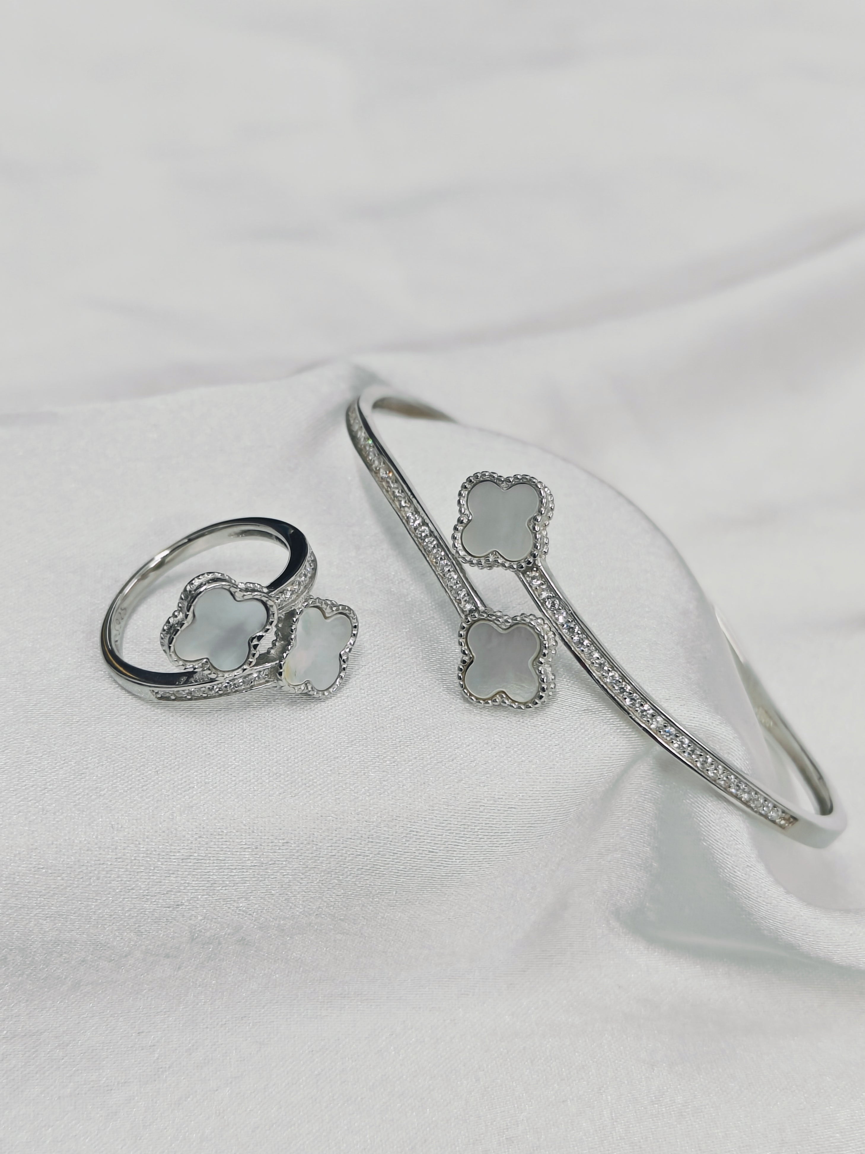 Silver ring and bracelet with clover designs on a white fabric background