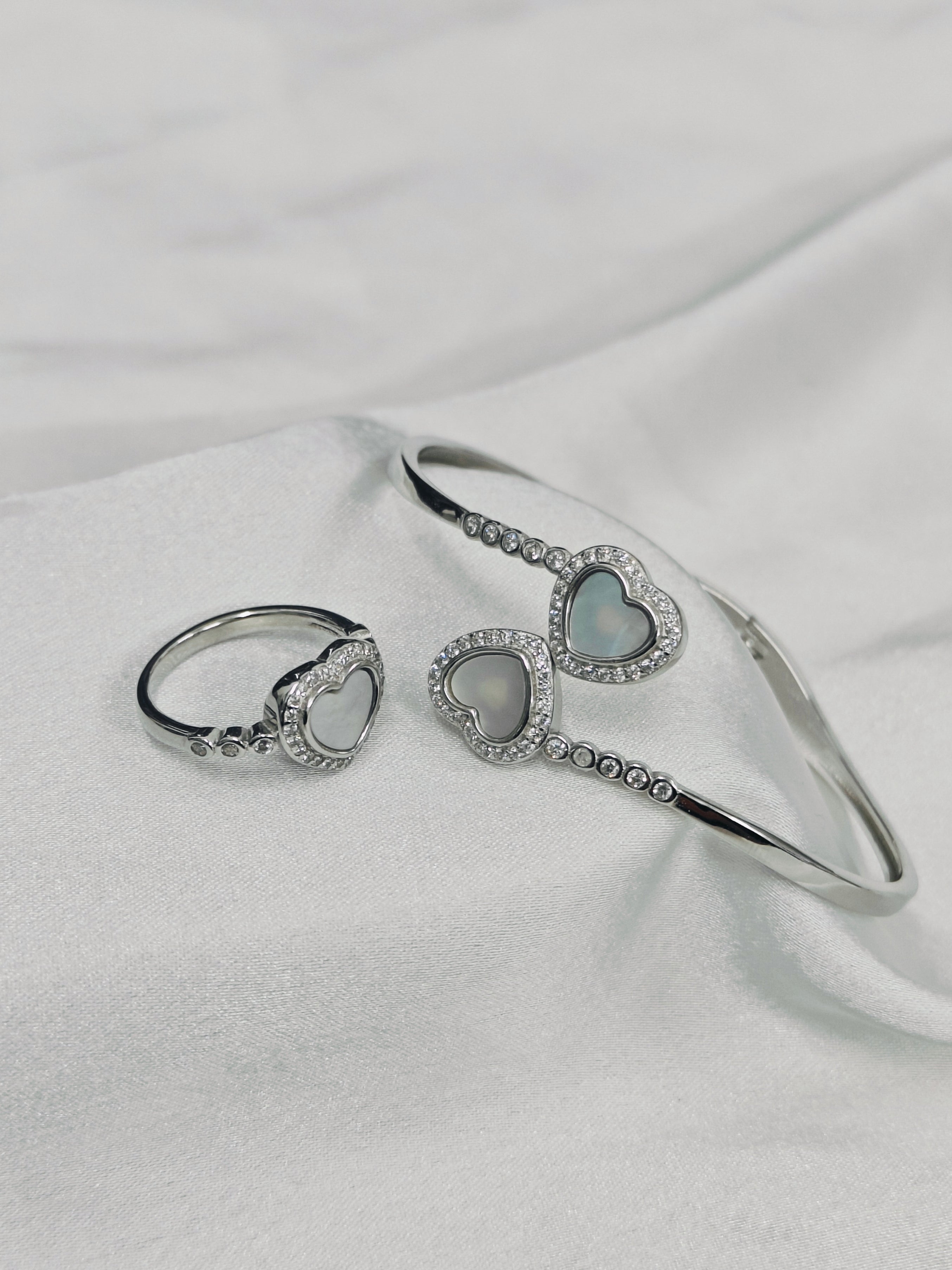 Silver bracelet and ring set with heart-shaped charms on a white fabric background