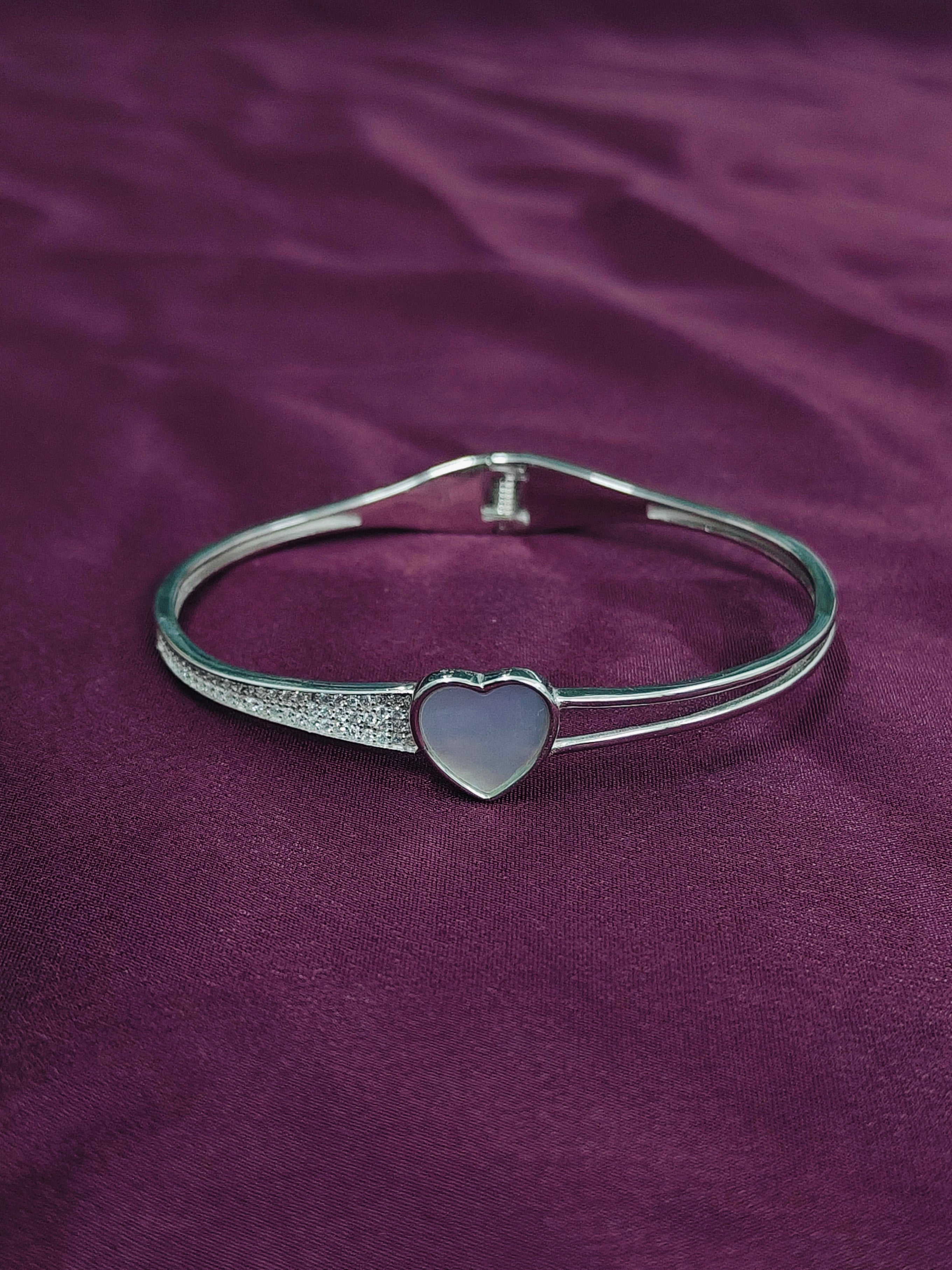 Silver bracelet with a heart-shaped clasp on a purple fabric background