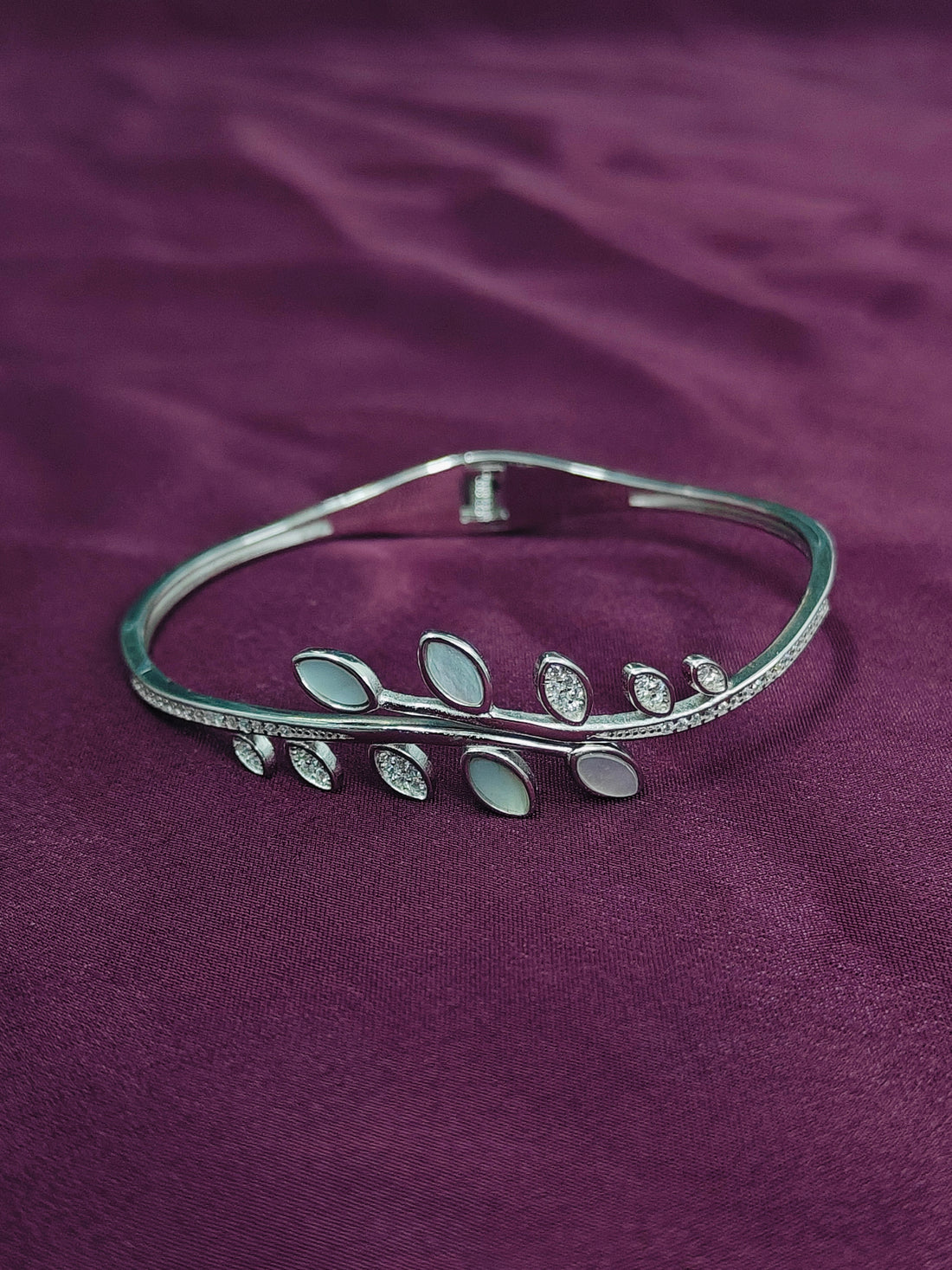 Silver bracelet with leaf design on a purple fabric background
