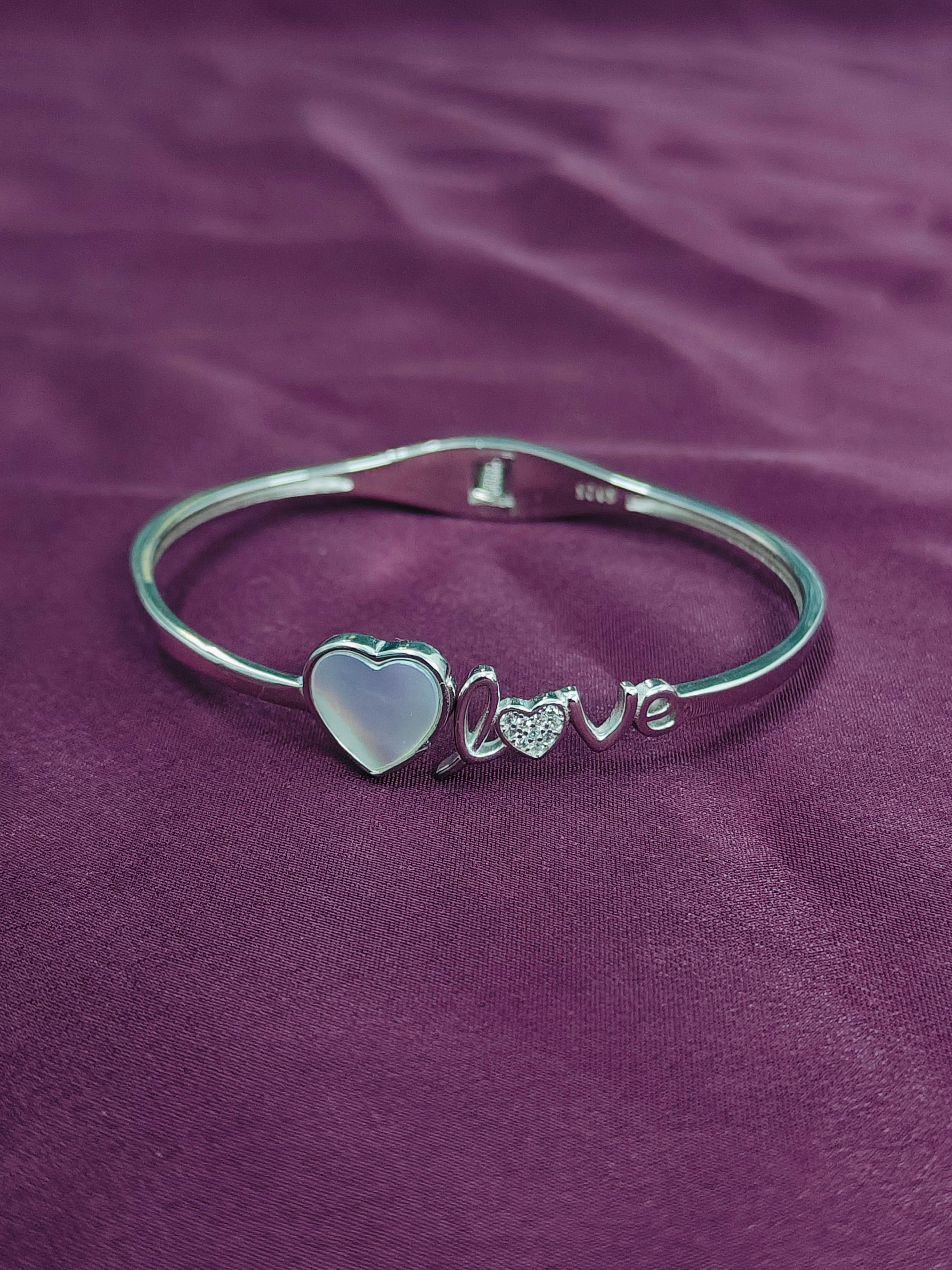 Silver bracelet with heart and 'love' charm on a purple fabric background