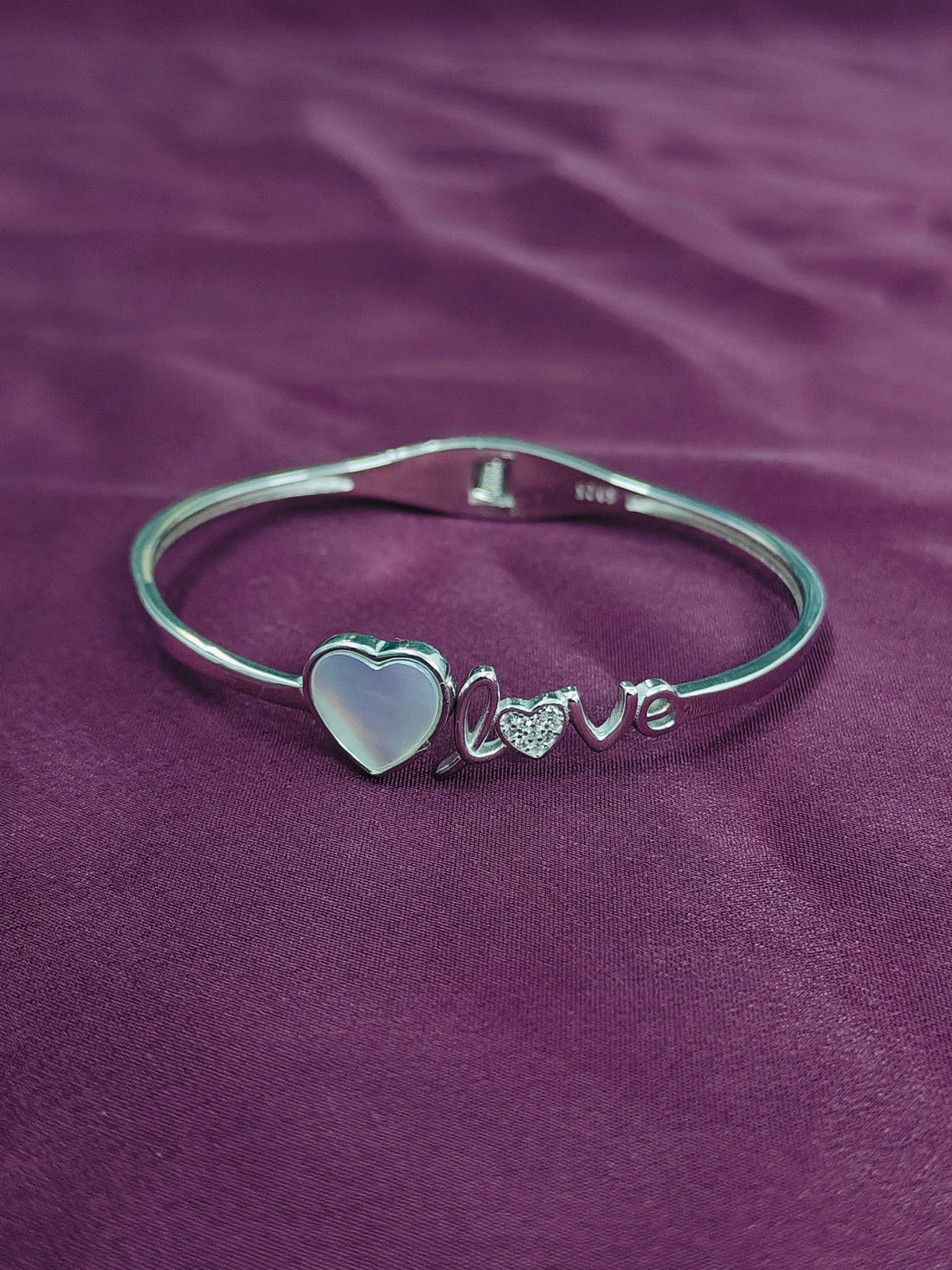 Silver bracelet with heart and 'love' charm on a purple fabric background