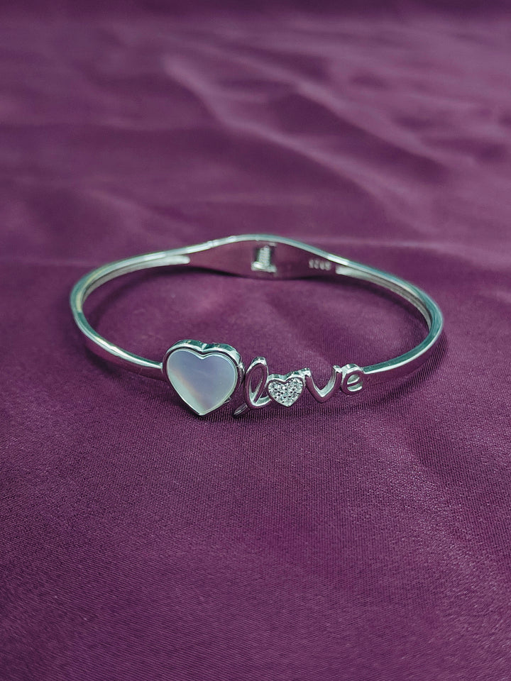 Silver bracelet with heart and 'love' charm on a purple fabric background