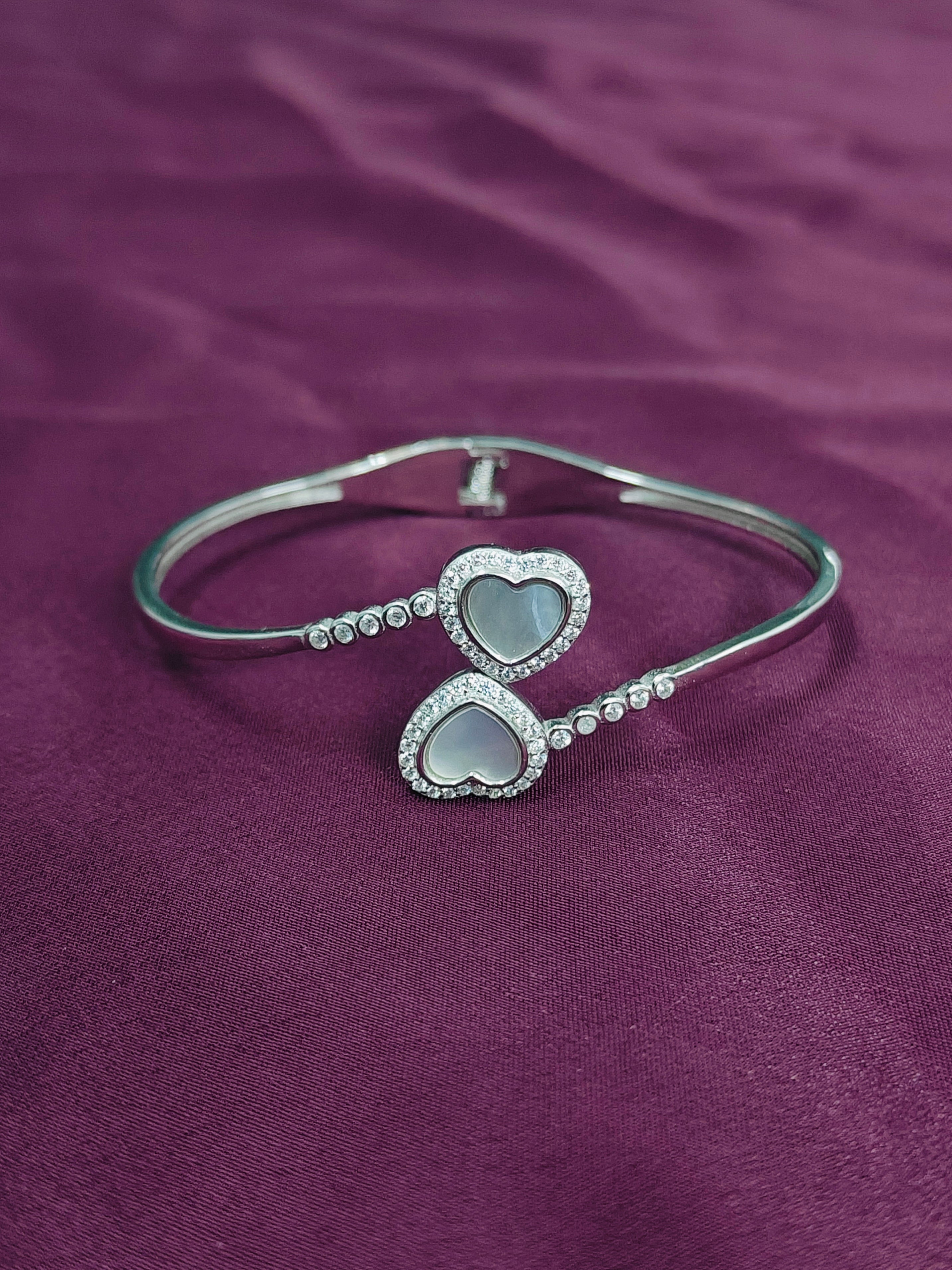 Silver bracelet with heart-shaped charms on a purple fabric background
