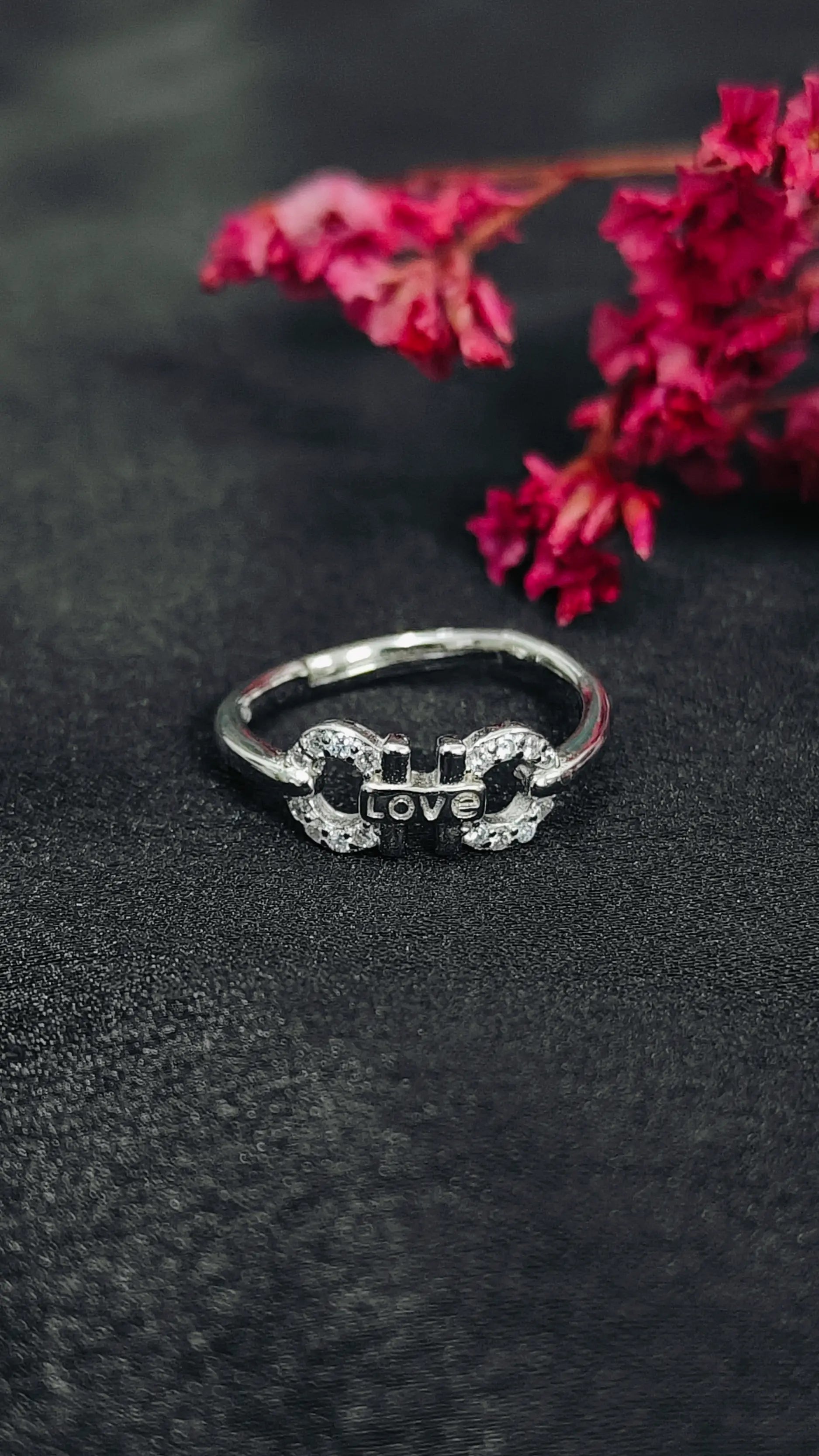 Silver ring with 'love' engraving on a dark surface with pink flowers.