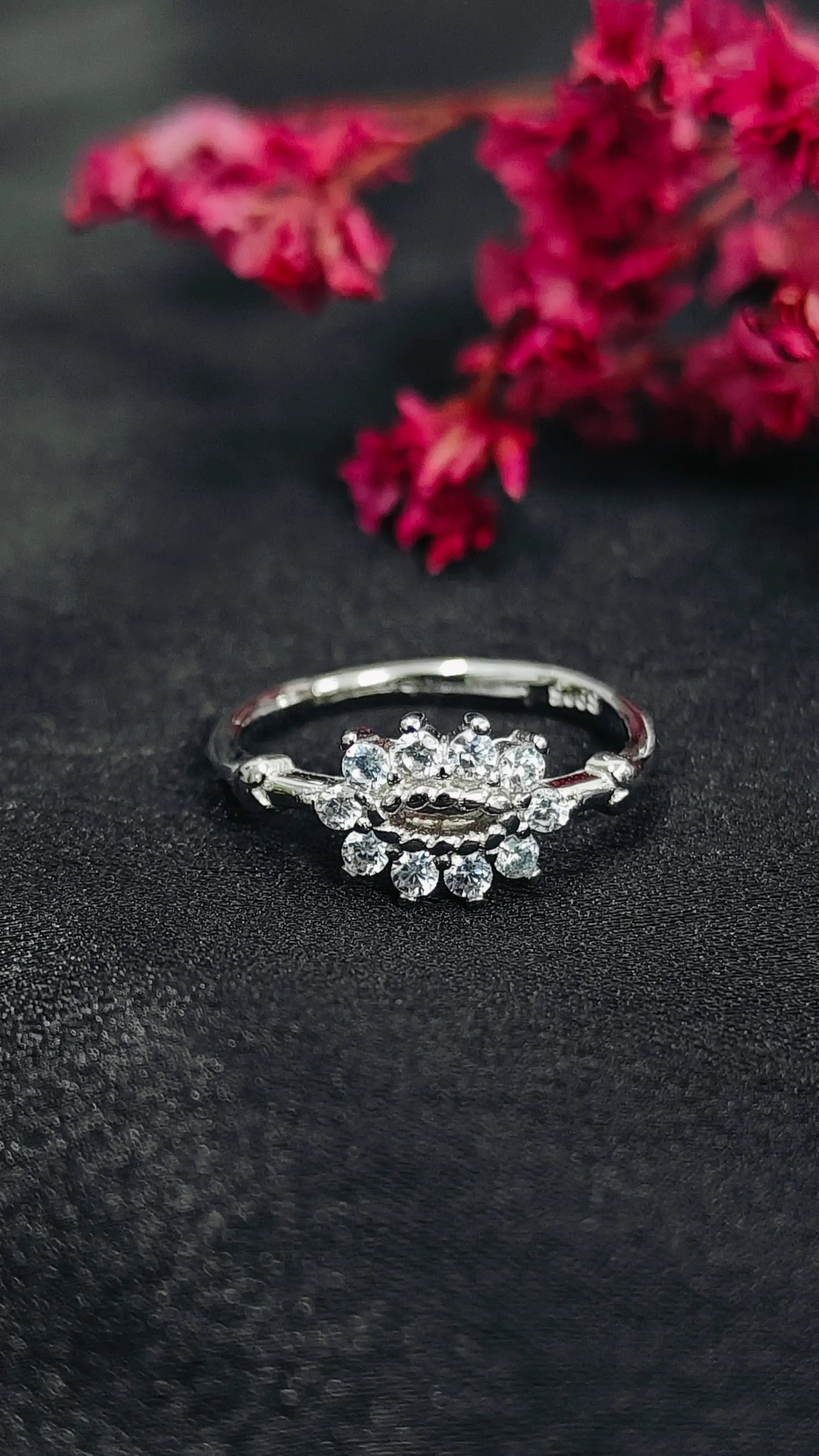 Silver ring with gemstones on a dark surface with pink flowers in the background