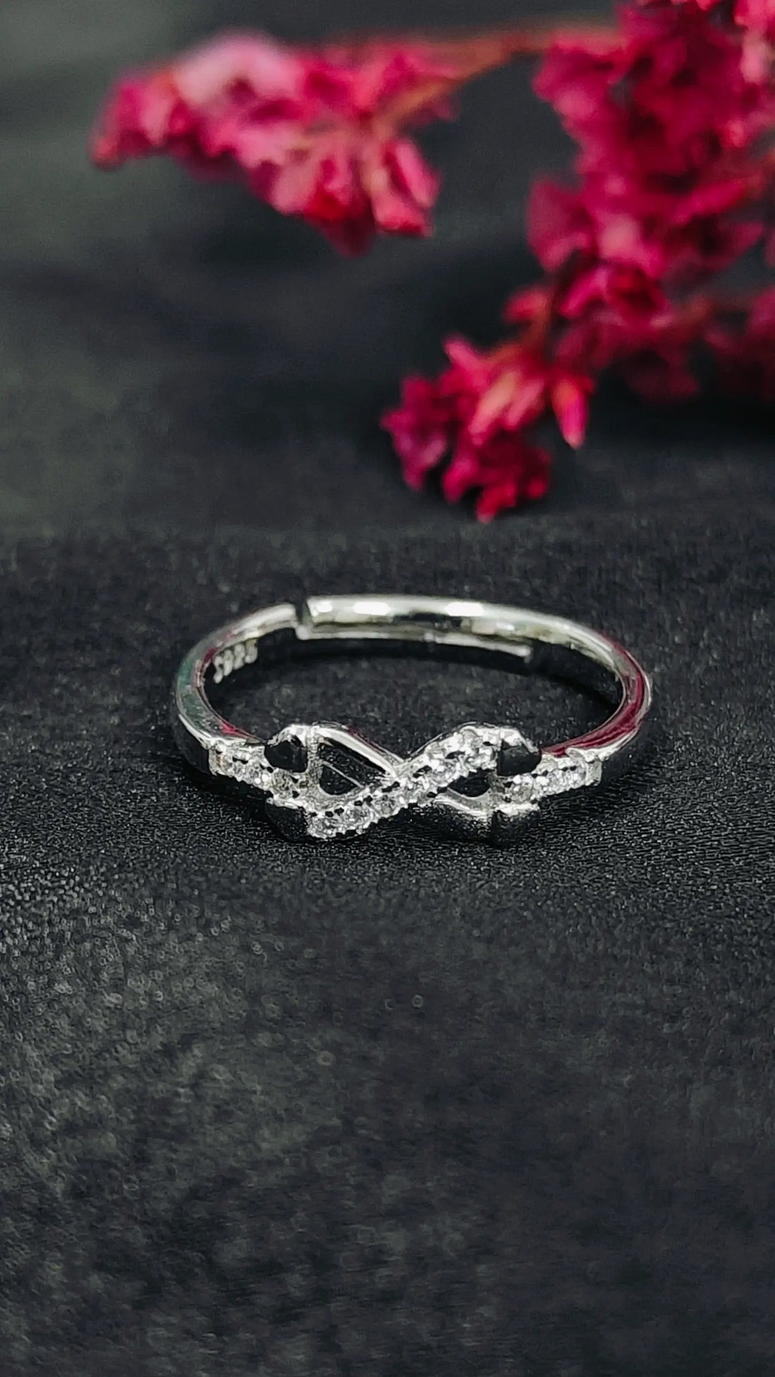 Silver infinity ring on a dark surface with pink flowers in the background
