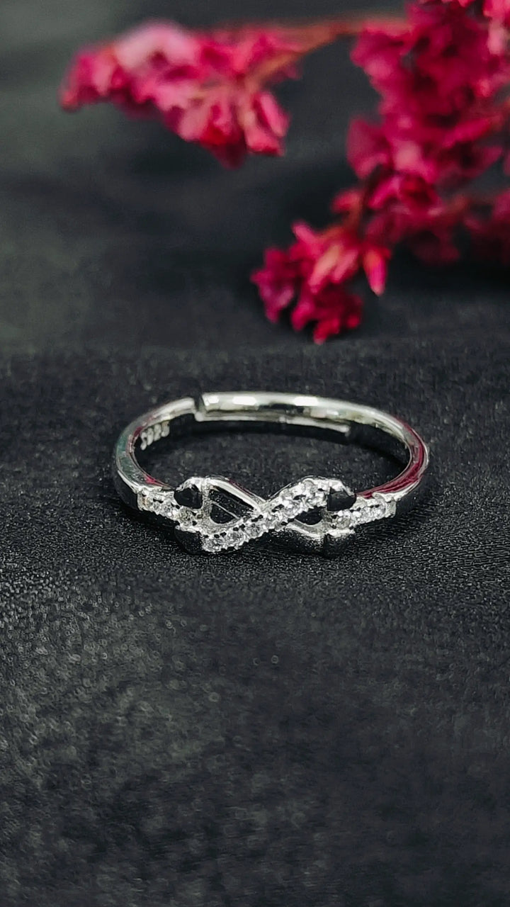 Silver infinity ring on a dark surface with pink flowers in the background