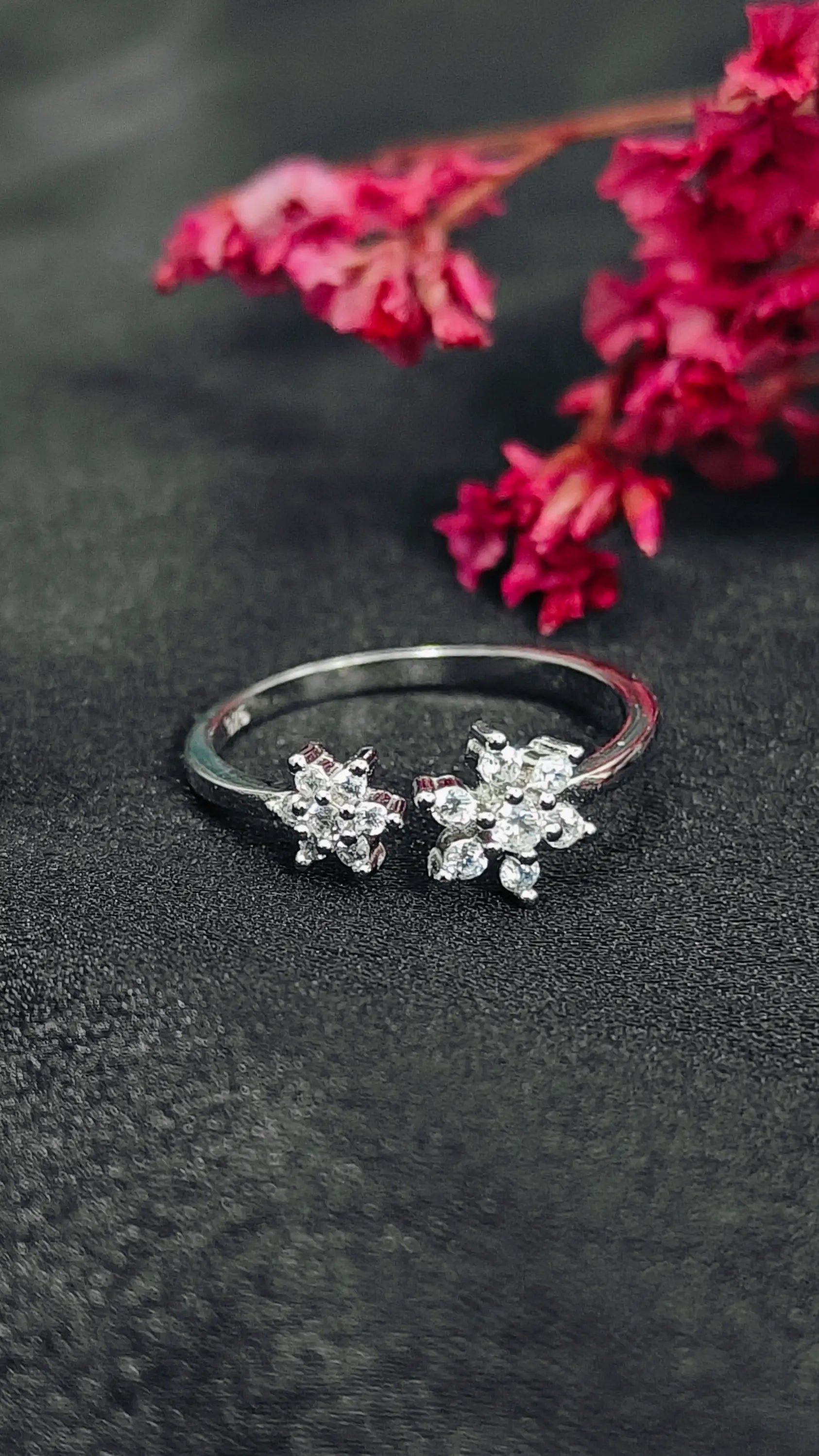 Silver ring with floral designs on a dark textured surface with pink flowers.